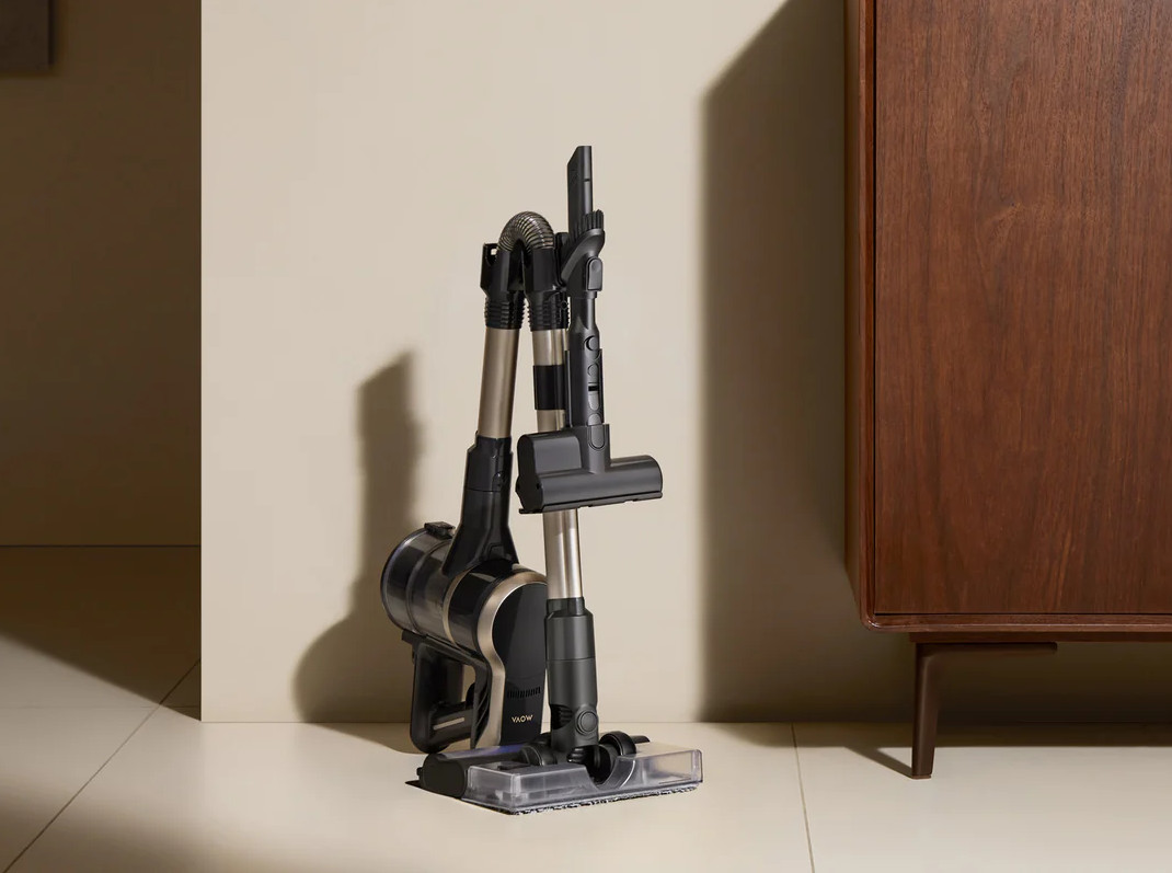 Czarny odkurzacz bezprzewodowy stoi na stacji ładującej obok drewnianej szafki.