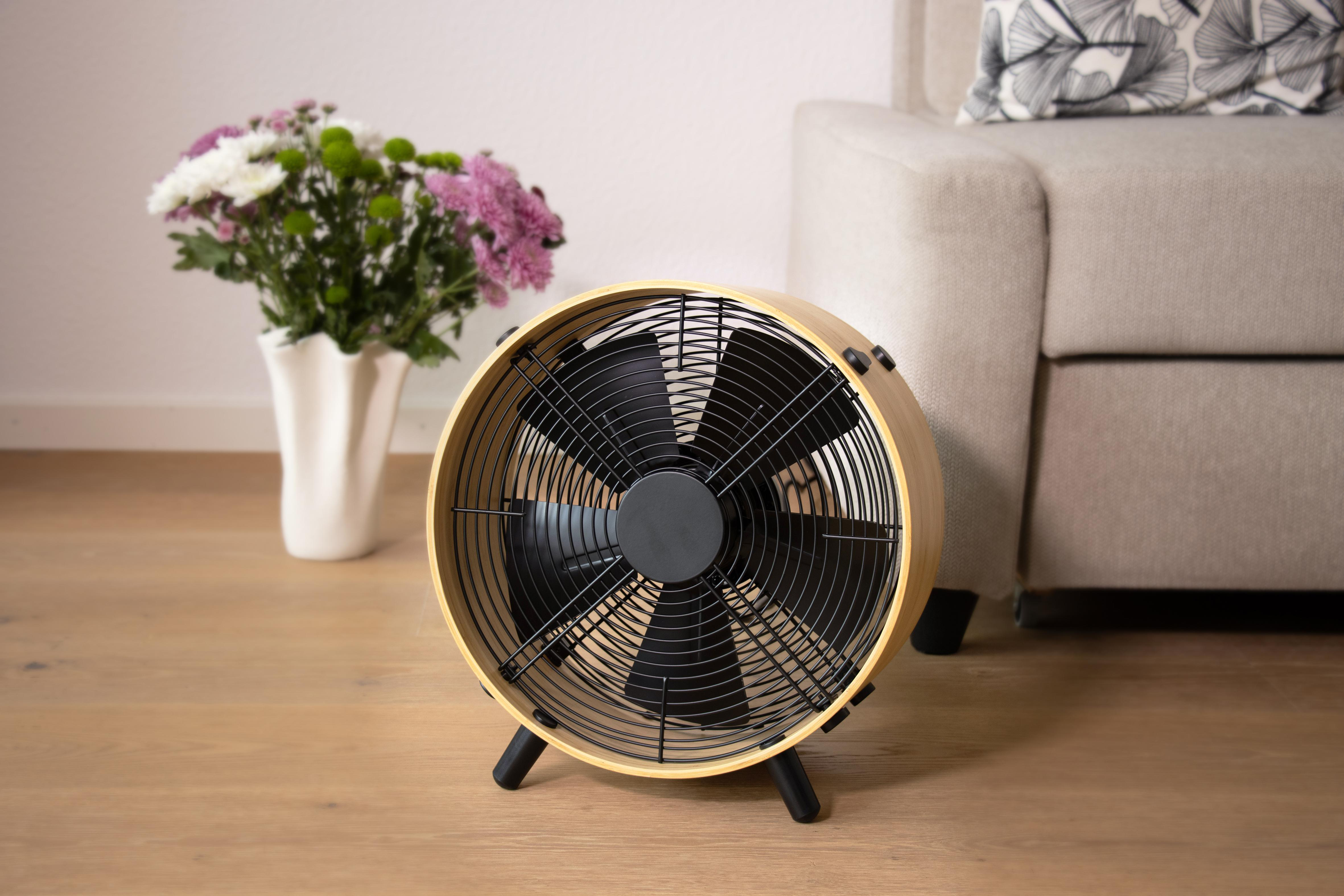 Ein Ventilator mit Holzrahmen steht auf einem Holzboden neben einem Sofa.