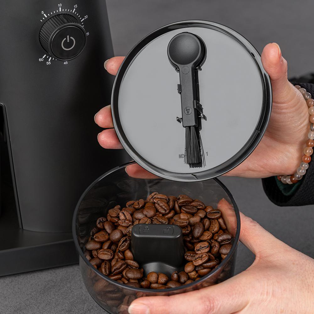 Kaffeebohnen in einem Behälter, Deckel mit Bürste und Löffel wird gehalten.