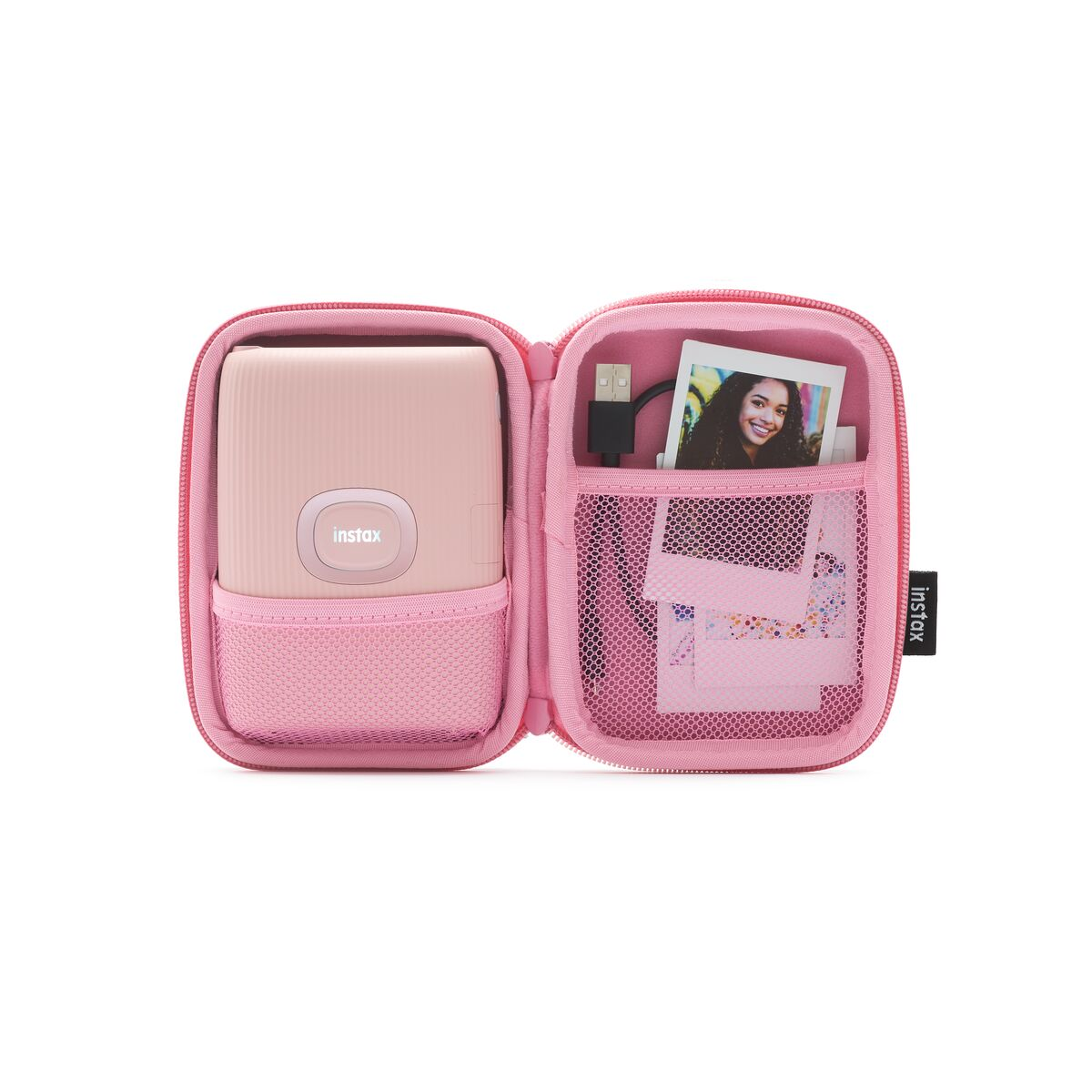 Açık pembe Instax kılıfı; kamera, kablo, fotoğraf ve aksesuarlar görünüyor.