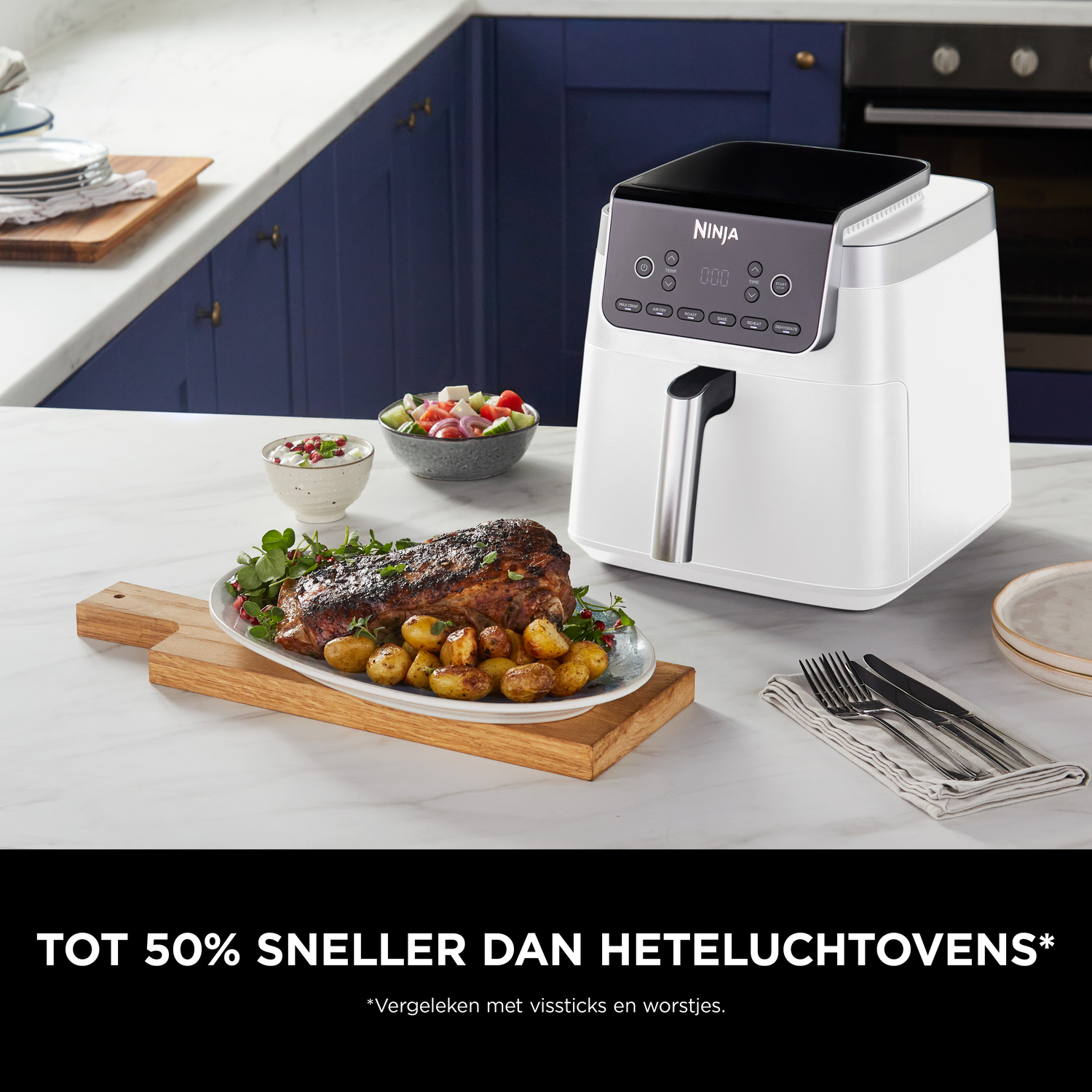 Een witte Ninja airfryer naast een gebraden vlees en aardappelen in een keuken.