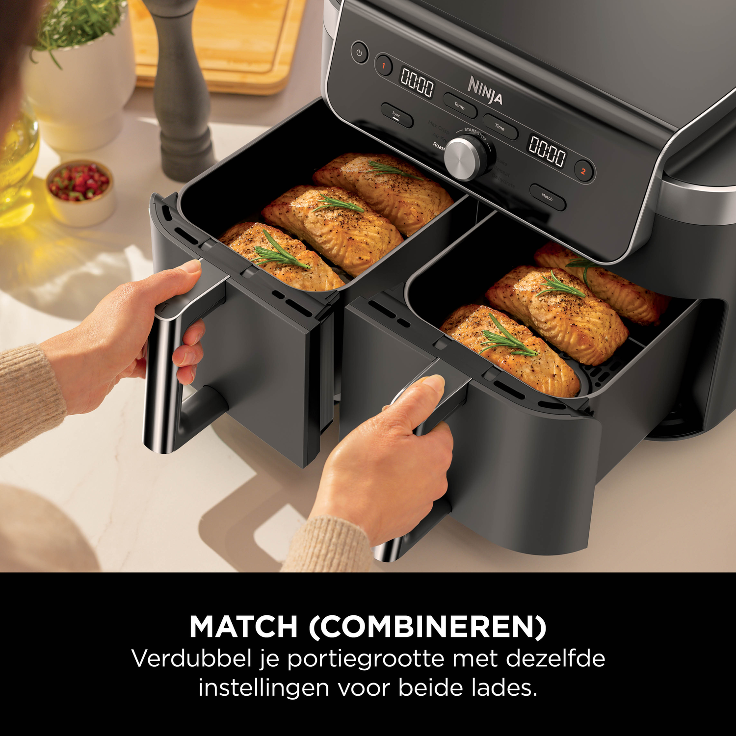 Twee lades van een zwarte airfryer gevuld met gekookte zalm en rozemarijn.