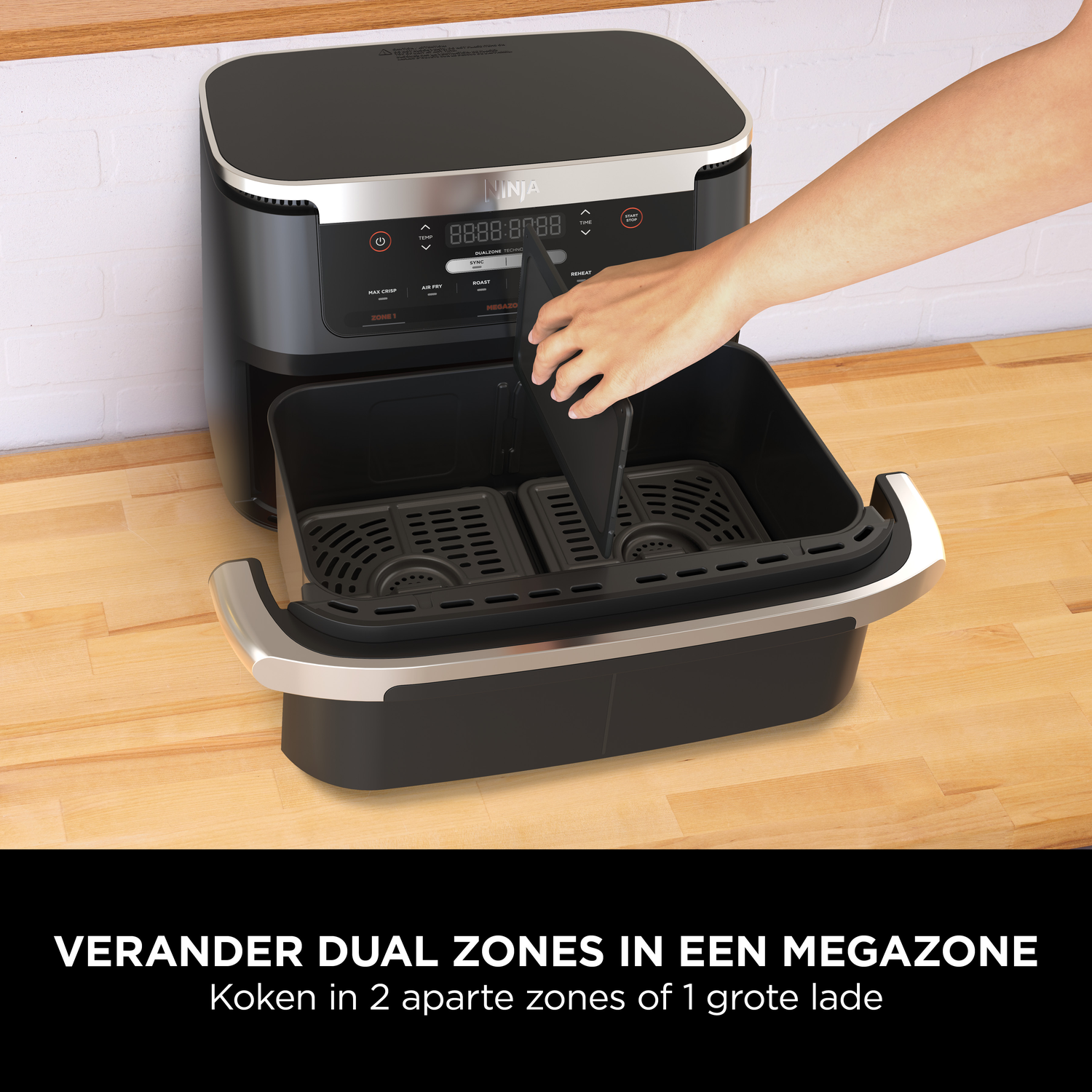 Een hand plaatst een scheidingswand in een zwarte airfryer met twee manden.
