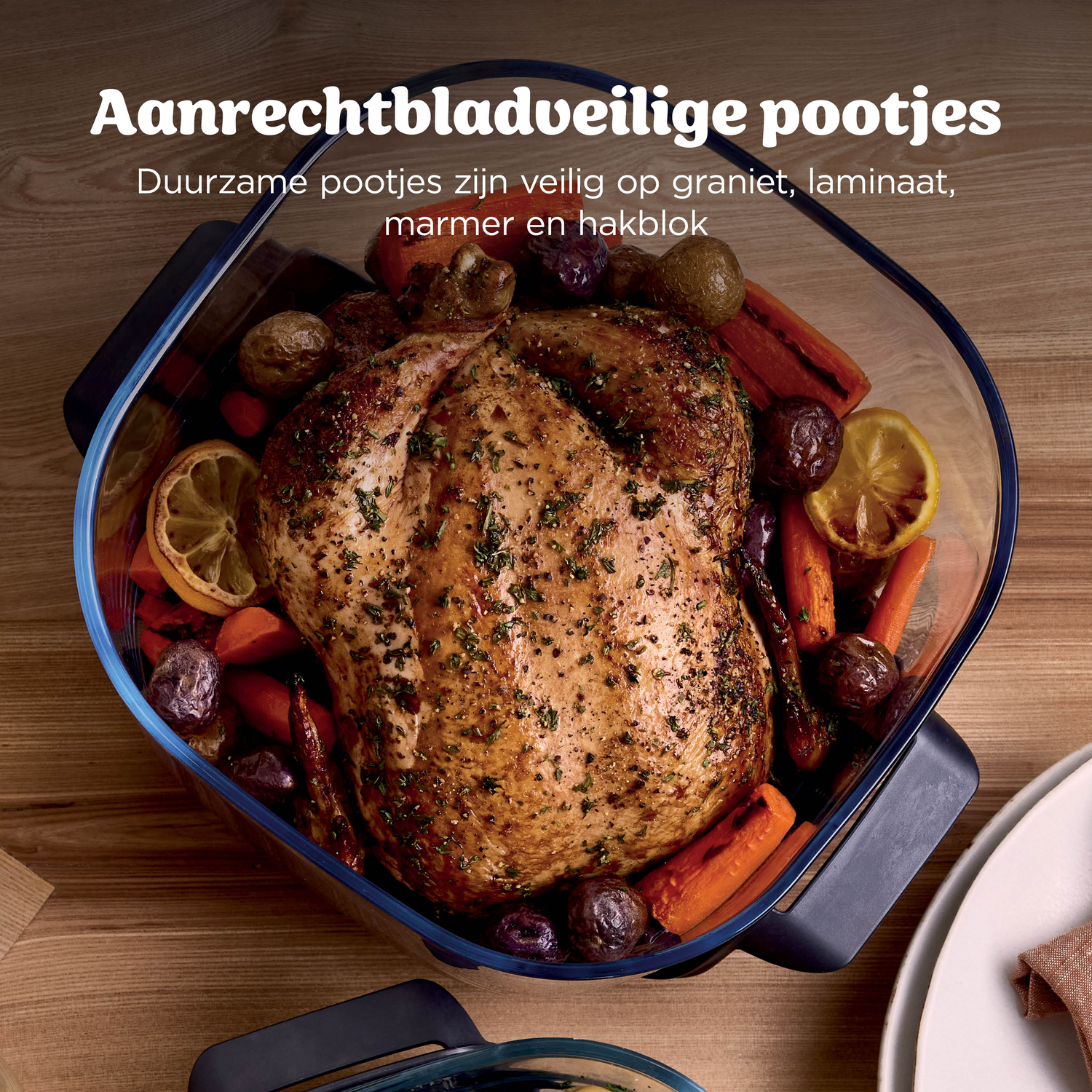Een geroosterde kip met wortels en aardappelen in een ovenschaal op houten tafel.