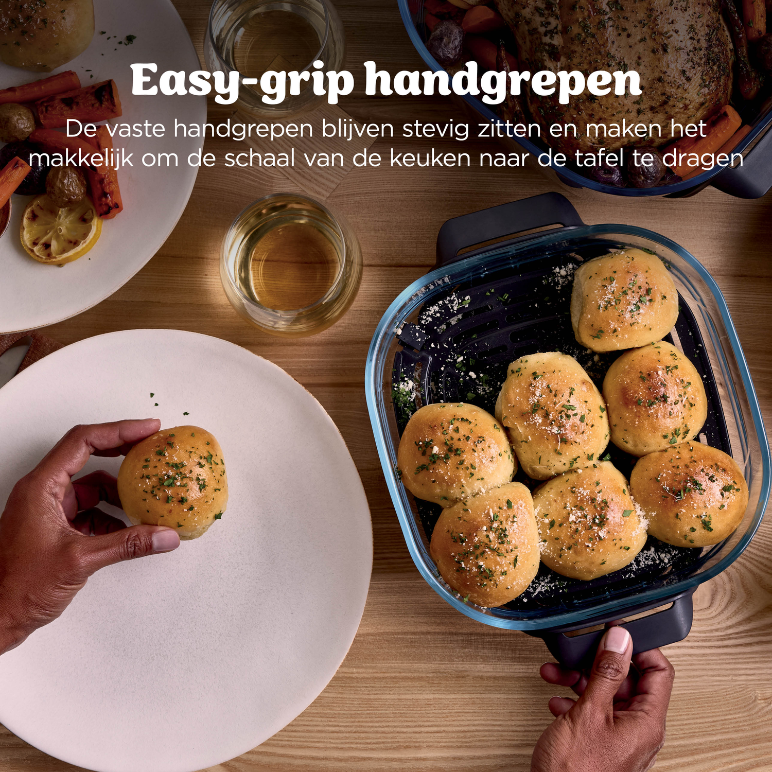 Een hand houdt een broodje op een bord, naast een ovenschaal met broodjes.