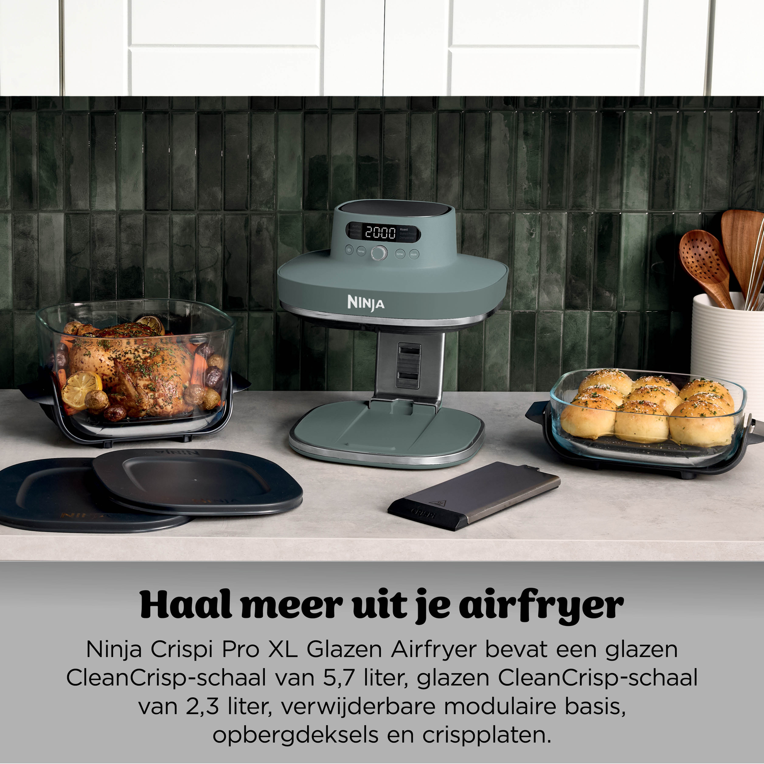 A roasted chicken with vegetables in a glass dish next to an air fryer and rolls.