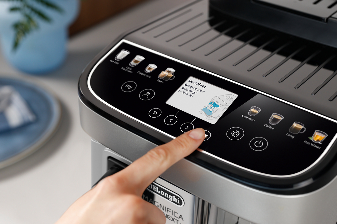 Eine Hand drückt auf den Knopf einer Kaffeemaschine, die „Entkalkung“ anzeigt.