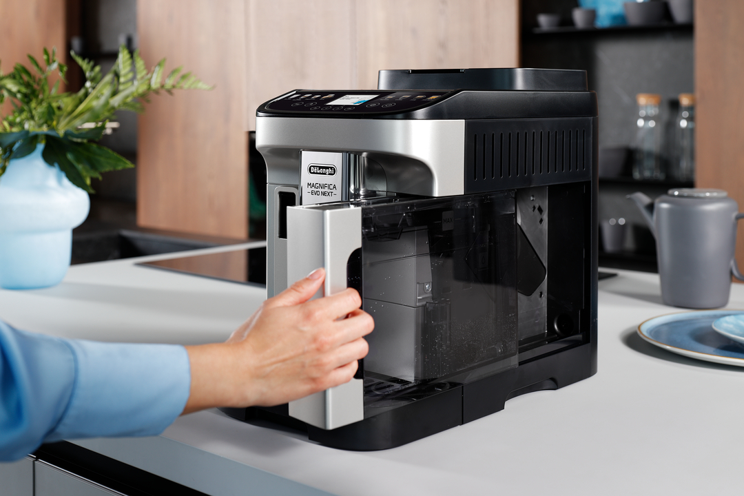Eine Hand öffnet den Wassertank einer Kaffeemaschine in einer Küche.