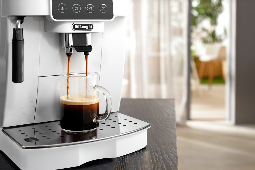 Eine weiße DeLonghi Espressomaschine brüht Kaffee in eine Glastasse.