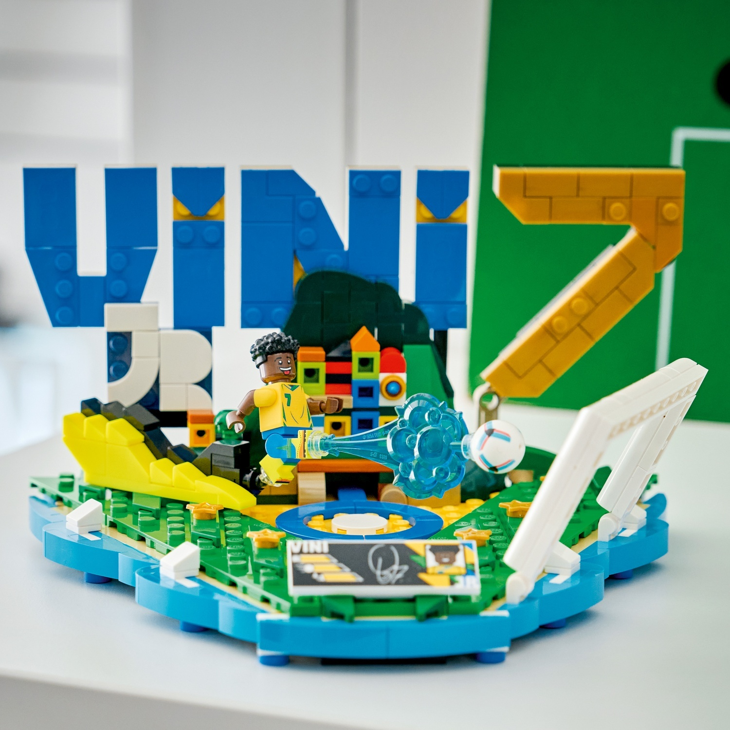 Statua Lego Vini Jr. con pallone e porta. Grandi lettere blu 'VINI' e giallo '7'.