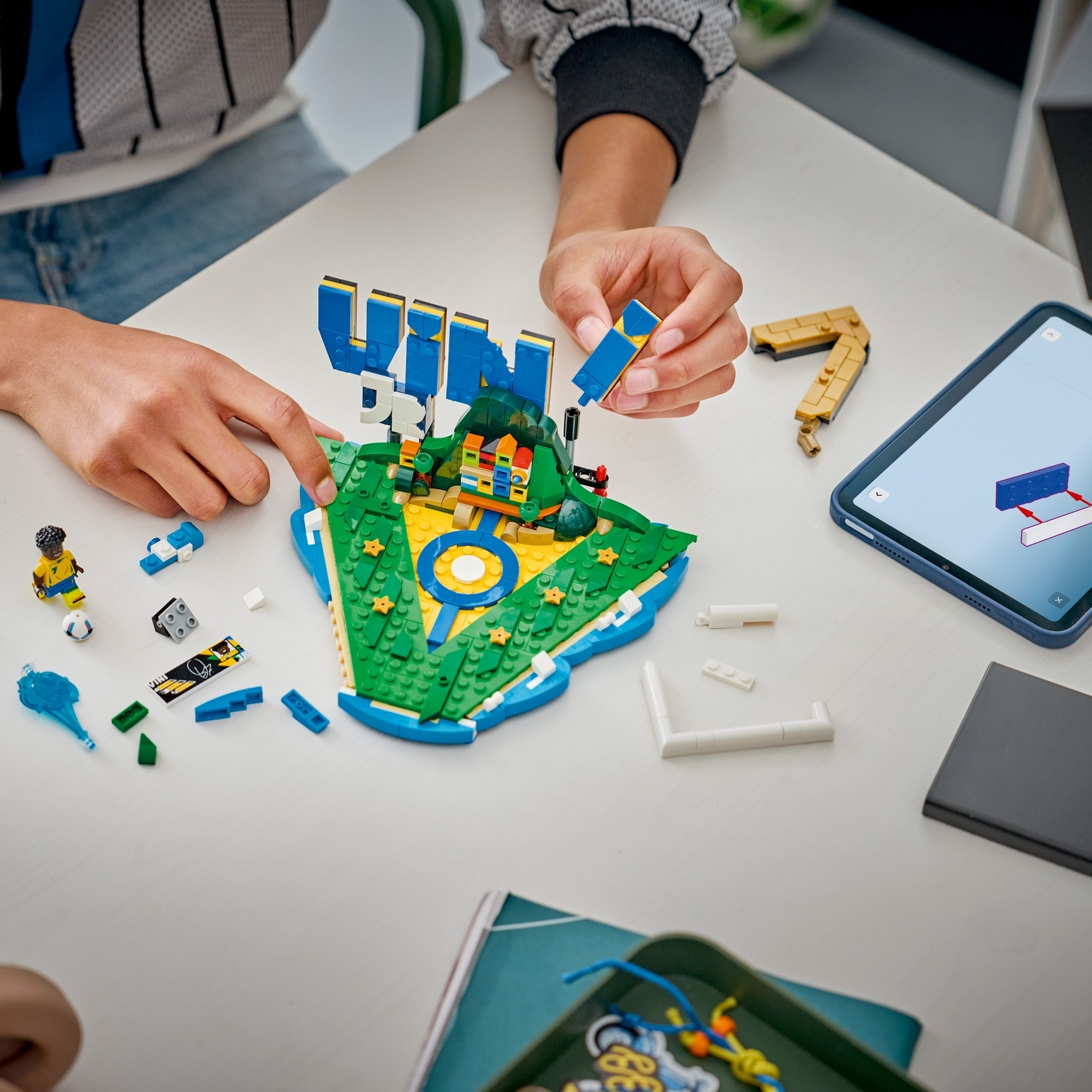 Mani che costruiscono un'isola Lego colorata con un tablet che mostra le istruzioni.