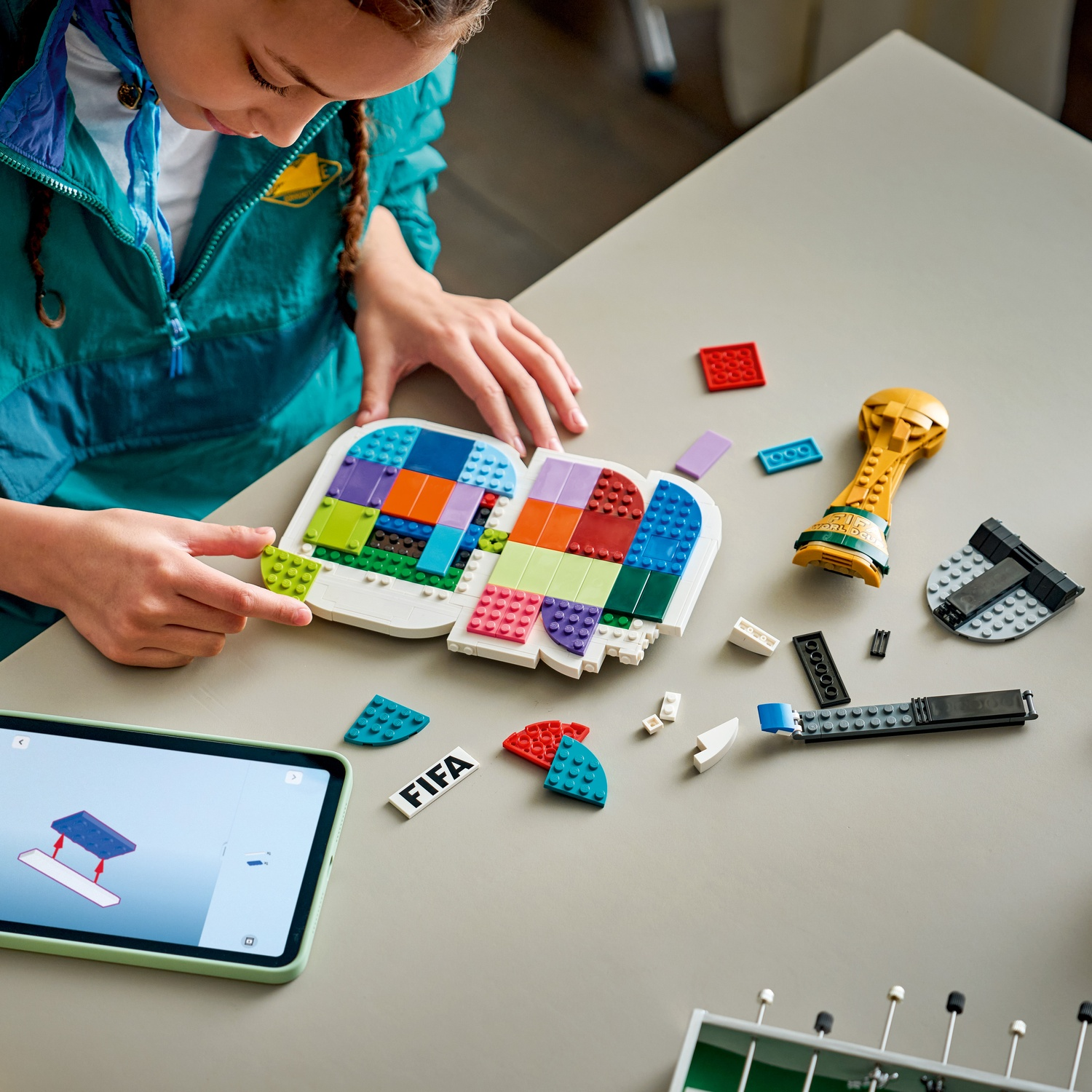 Una bambina costruisce con mattoncini Lego colorati, istruzioni su un tablet.