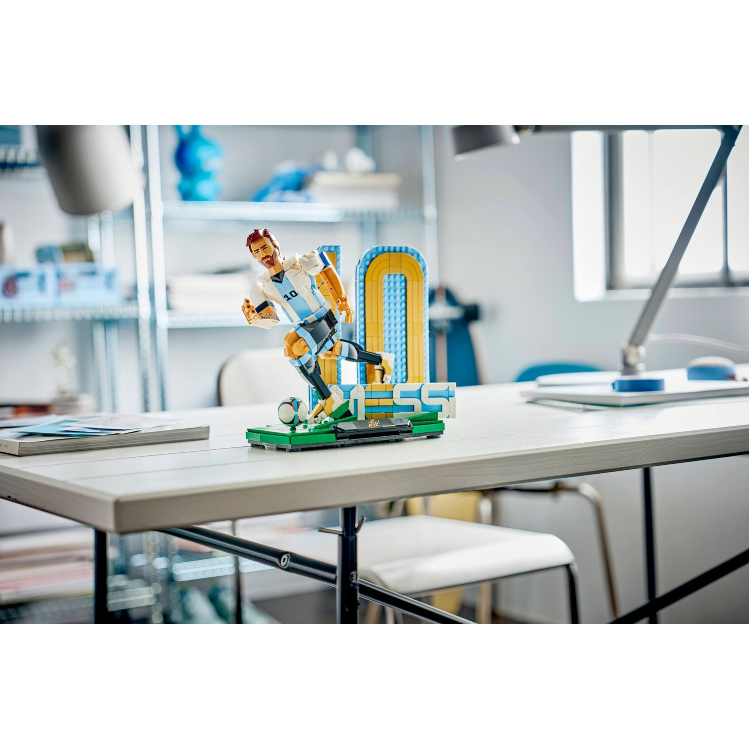 Figura Lego di Lionel Messi in azione, su una scrivania con lampada e scaffali.