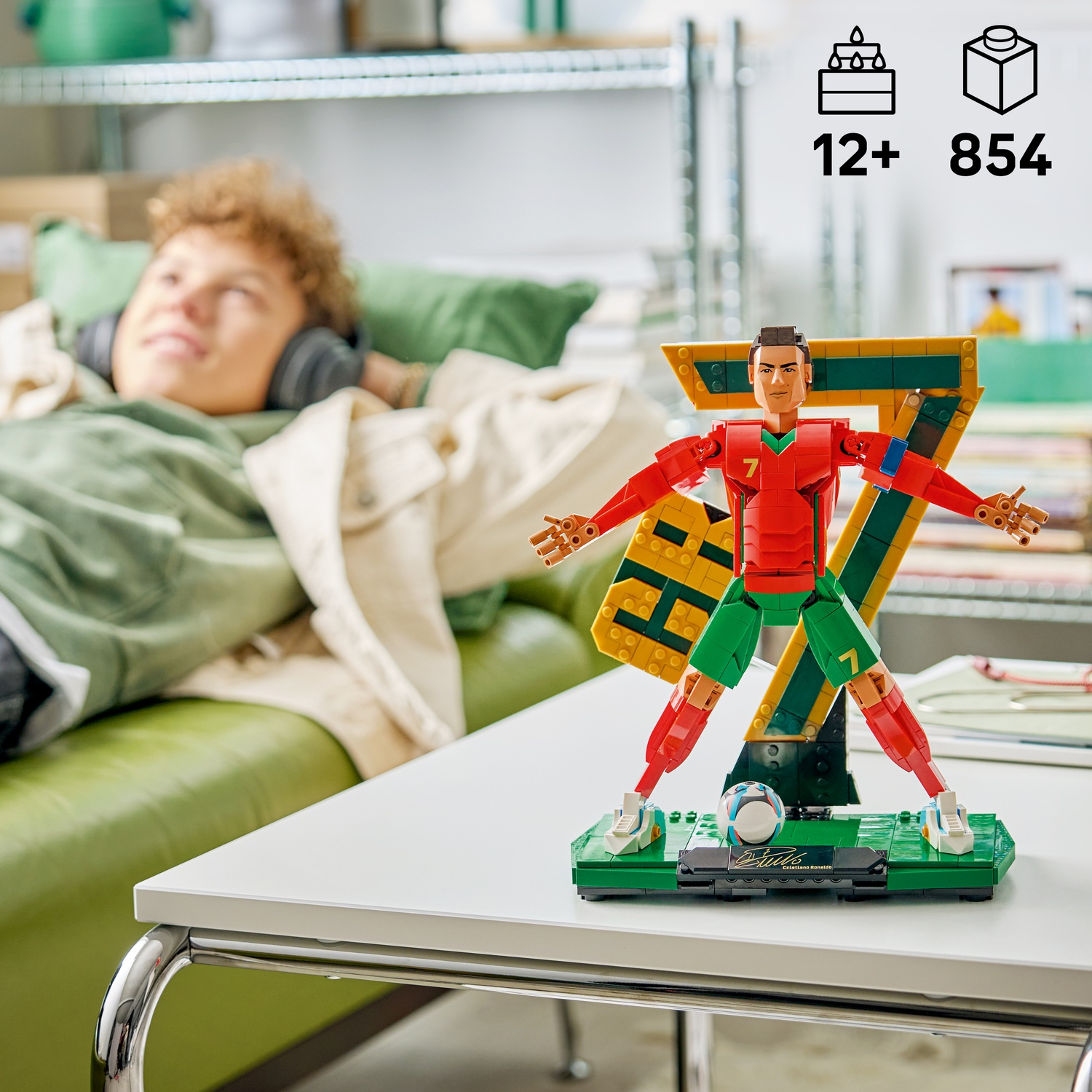 Un ragazzo con cuffie giace su un divano. Accanto a lui un modello Lego di Cristiano Ronaldo.