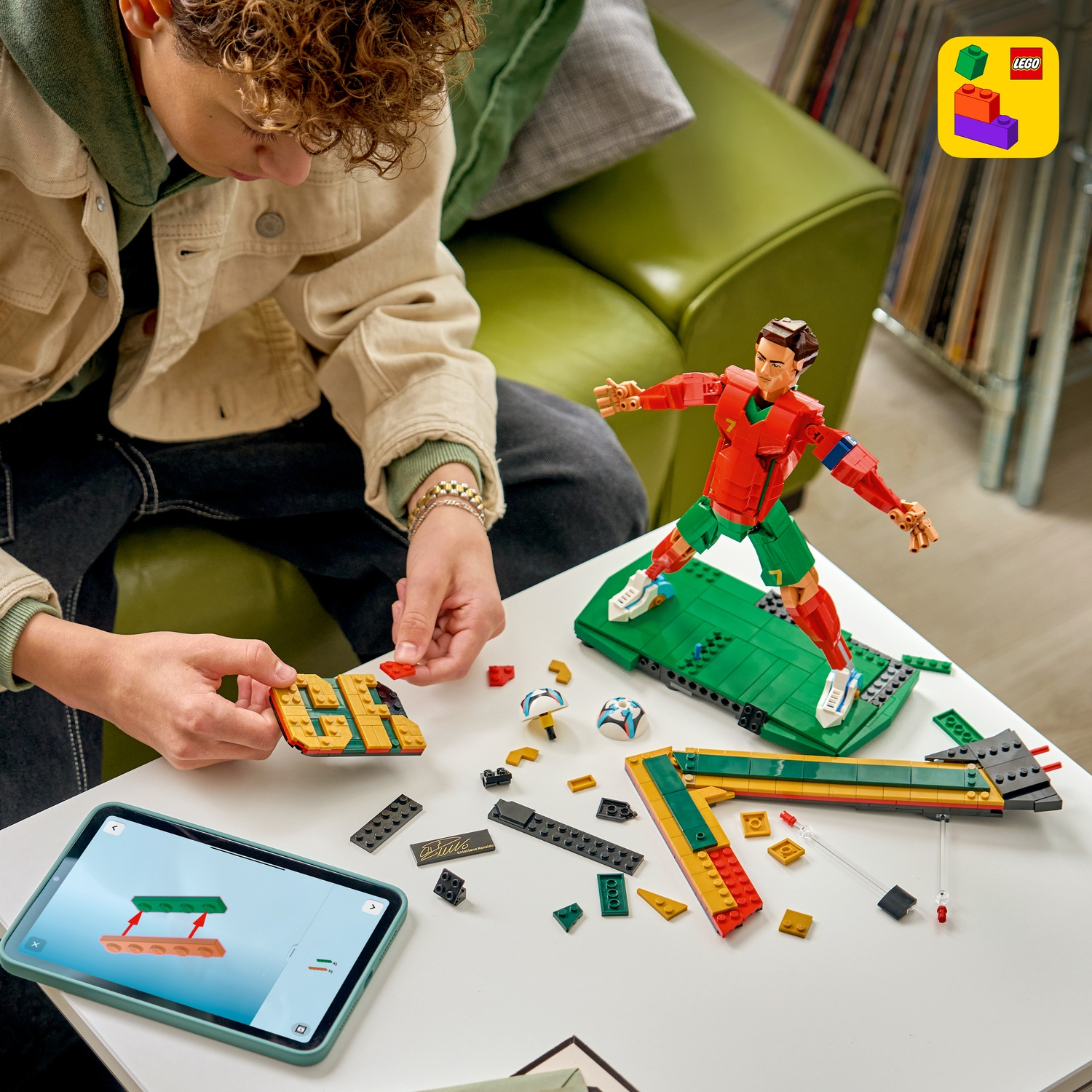 Una persona costruisce una figura LEGO di Cristiano Ronaldo su un tavolo con un tablet che mostra le istruzioni.