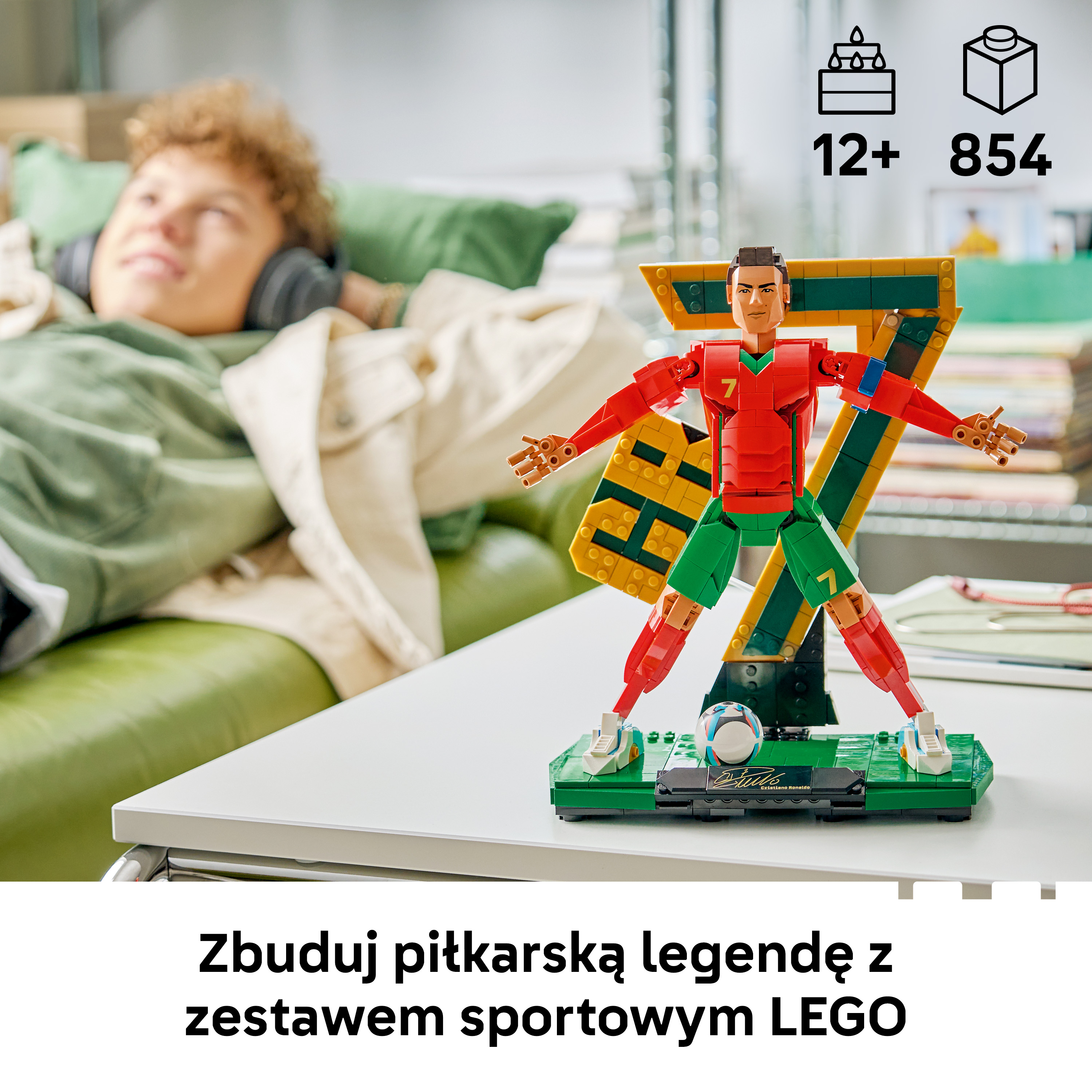Model piłkarza LEGO stoi obok chłopca w słuchawkach na kanapie.