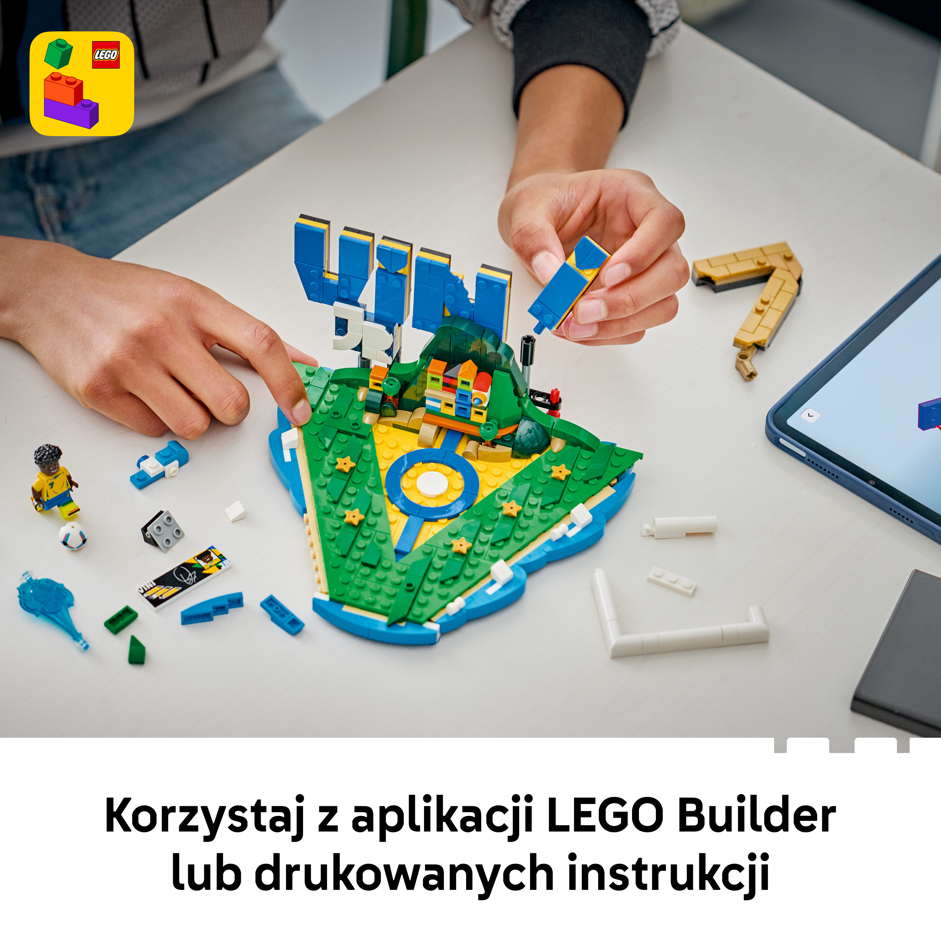 Ręce budują z klocków LEGO na stole, obok tabletu.
