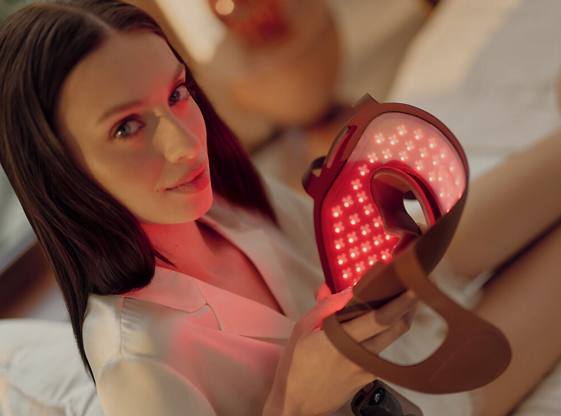 Kobieta trzyma maskę do terapii czerwonym światłem blisko twarzy.