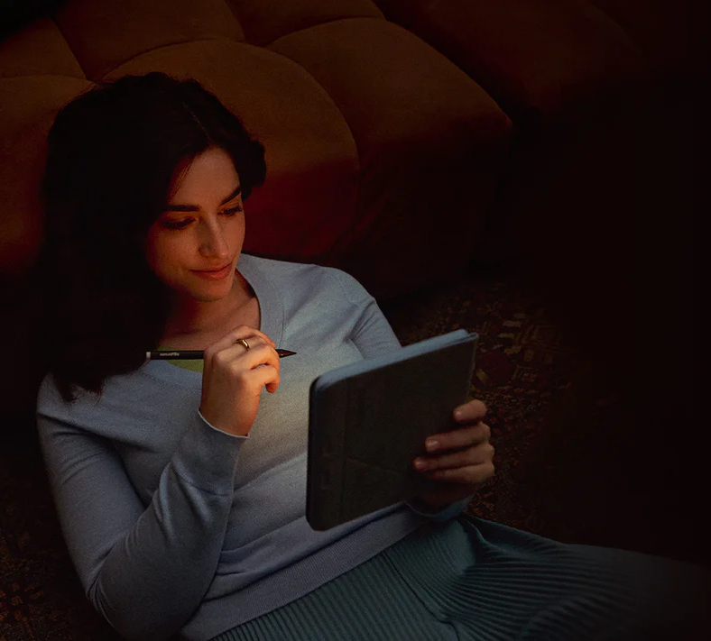 Kobieta z ciemnymi włosami pisze na tablecie w słabo oświetlonym pokoju.