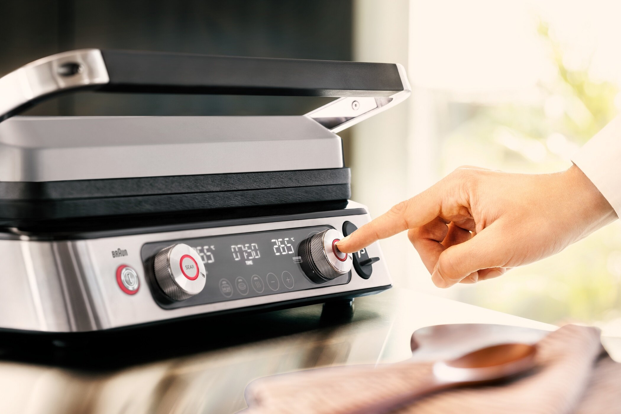 Dłoń naciska przycisk grilla Braun z cyfrowym wyświetlaczem.