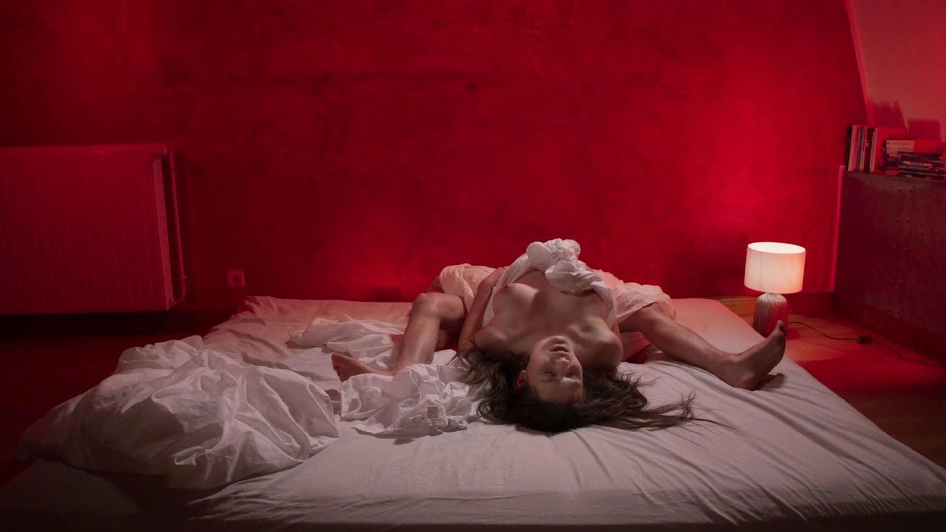 Ein Paar liegt in einem rot beleuchteten Schlafzimmer auf einem zerwühlten Bett.