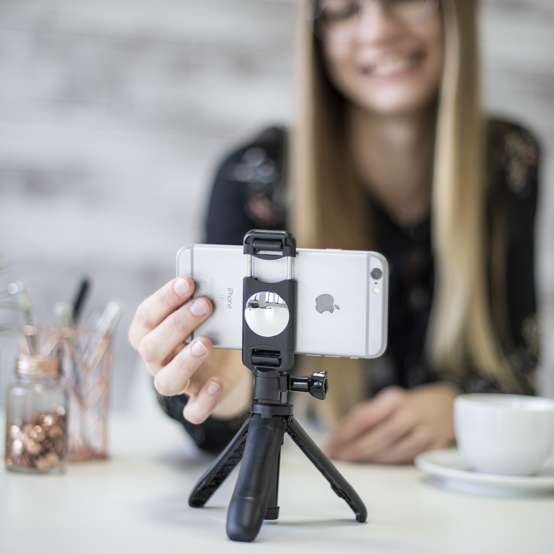 Uzun sarı saçlı bir kadın, küçük bir tripod üzerinde iPhone tutuyor.