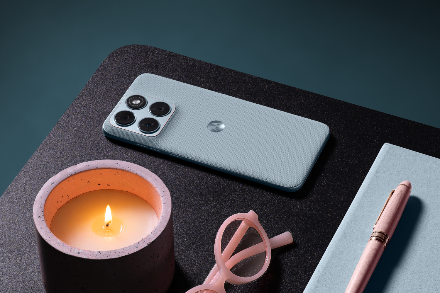 Jasnoniebieski telefon z czterema aparatami leży obok zapalonej świecy.