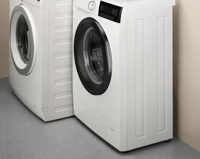 Dwie białe pralki stoją obok siebie na szarej podłodze.