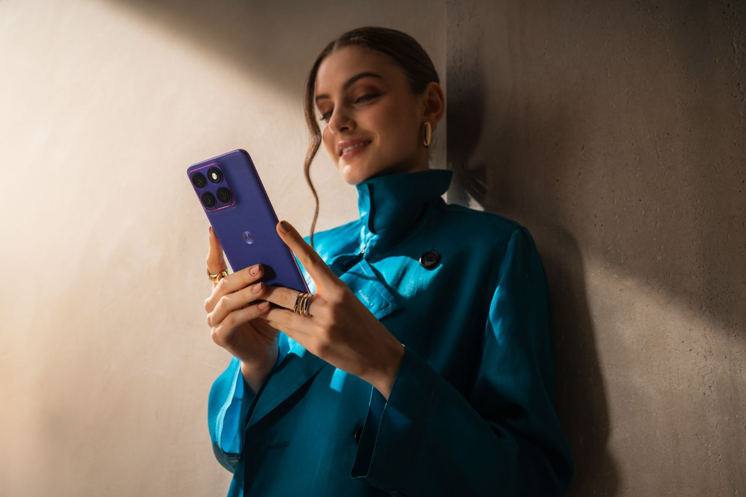Kobieta w niebieskim płaszczu trzyma fioletowy smartfon.