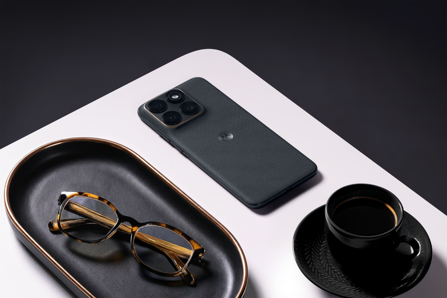 Ciemnoszary smartfon z czterema aparatami, obok okularów i filiżanki kawy.