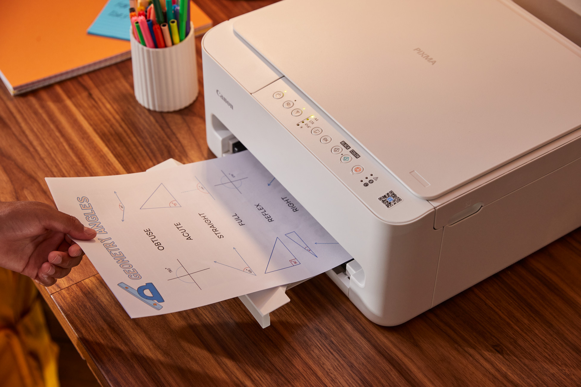Dłoń wyciąga kartkę z kątami geometrycznymi z białej drukarki Canon.
