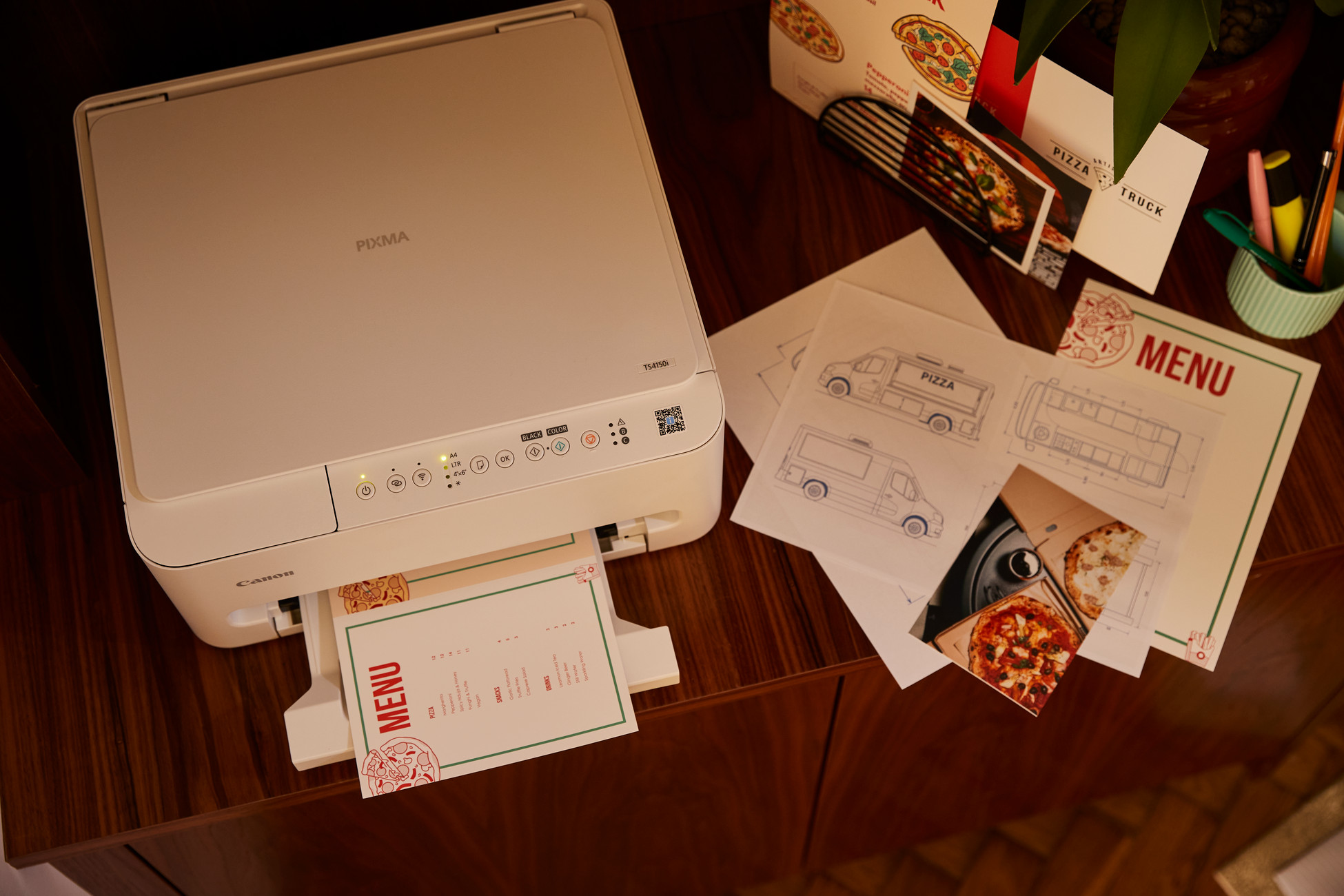 Biała drukarka Canon drukuje menu z ilustracjami pizzy.