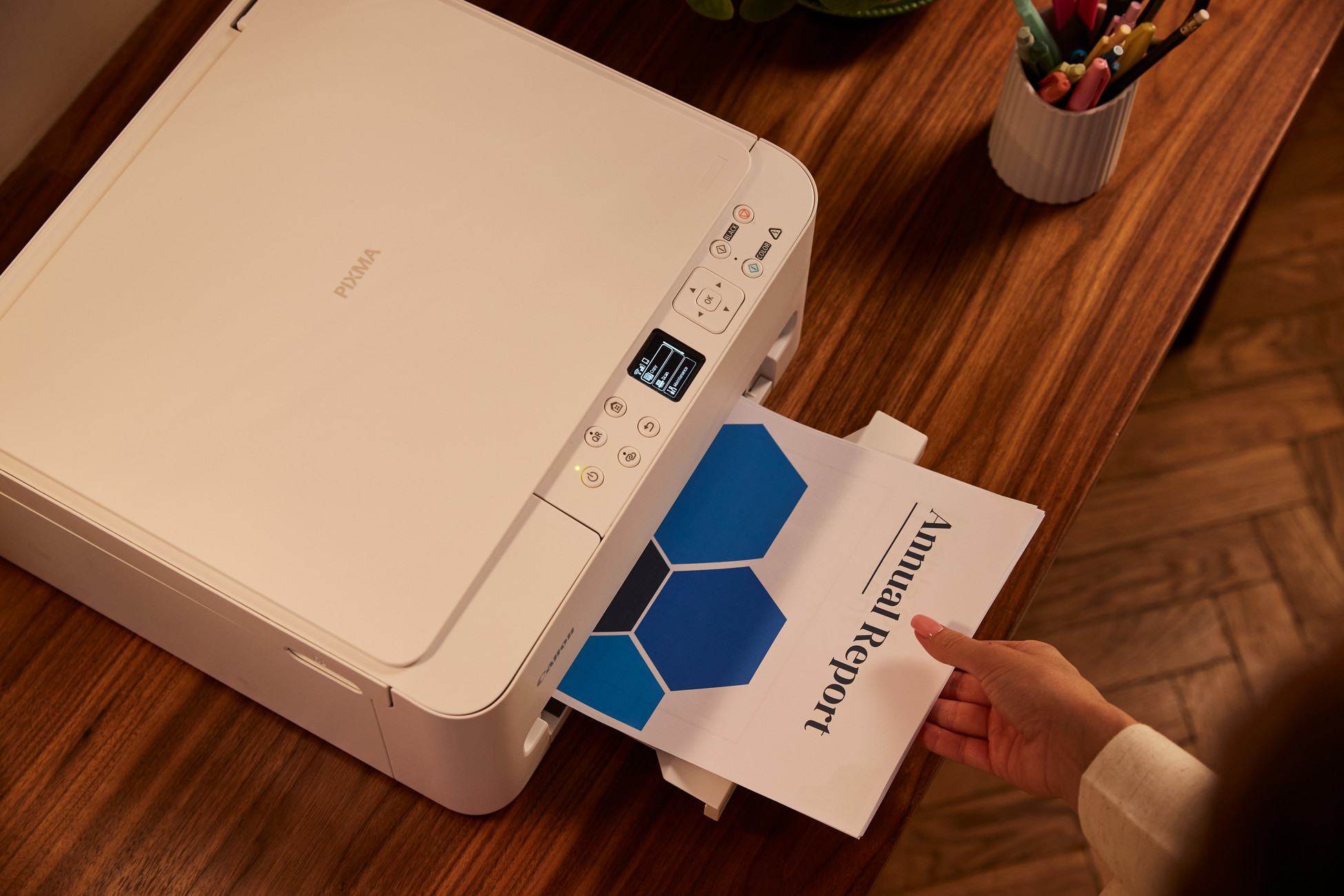 Biała drukarka Canon PIXMA drukuje raport roczny z niebieskimi sześciokątami.
