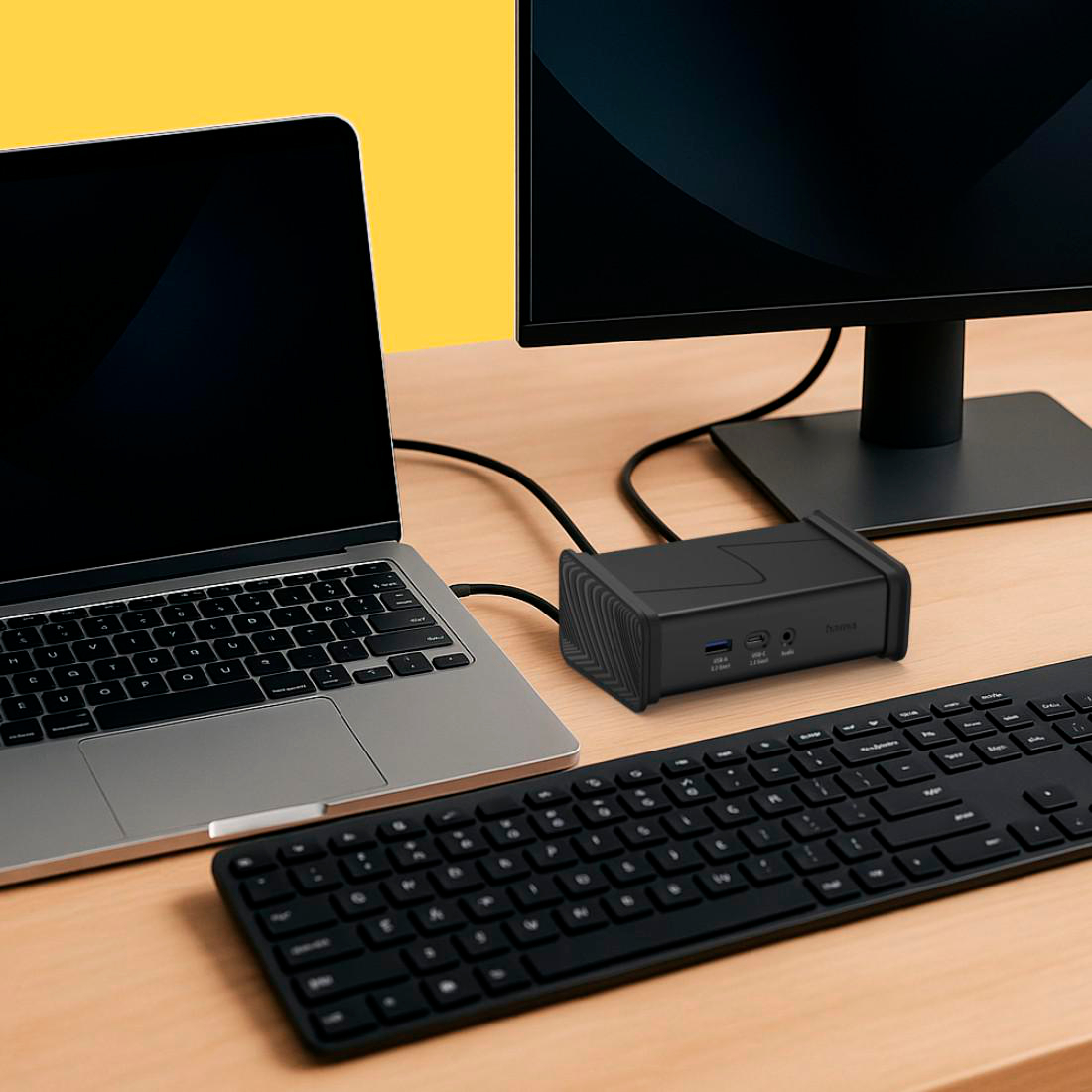 Ein Laptop, eine Dockingstation, eine Tastatur und ein Monitor stehen auf einem Holztisch.