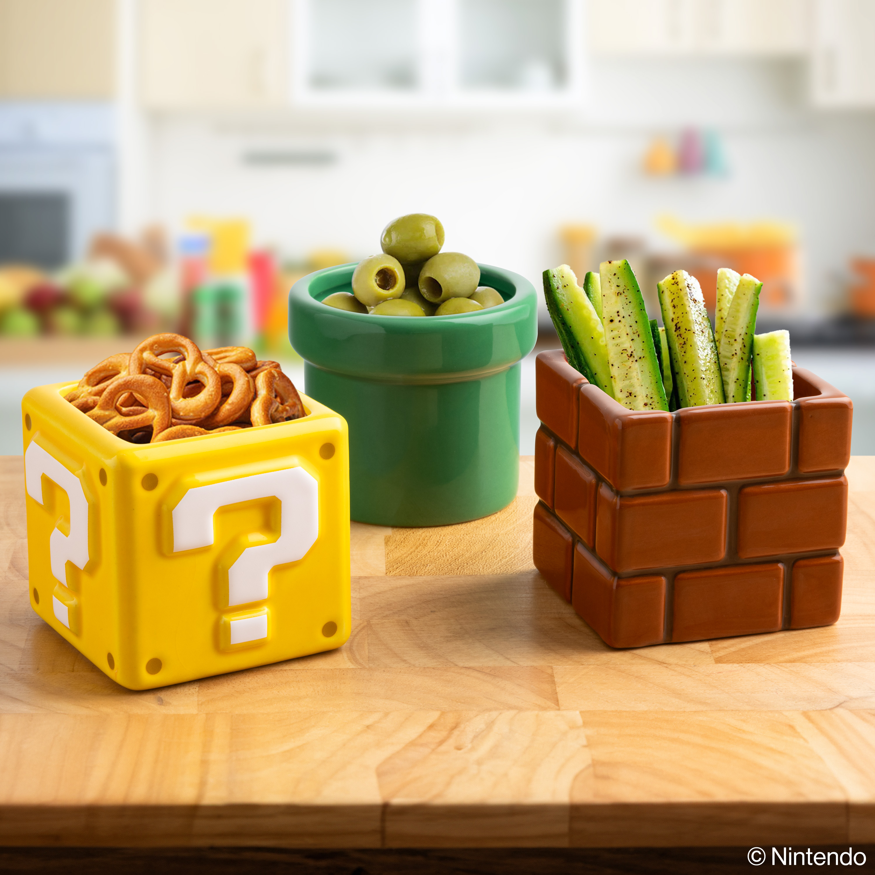 Drei Behälter mit Snacks: Brezeln, Oliven und Gurkensticks auf Holztisch.
