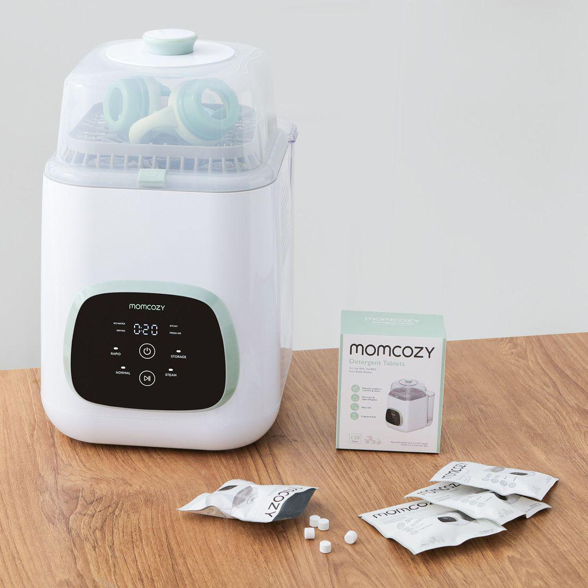 Ein weißer Sterilisator mit grünem Deckel, daneben eine Box mit Spülmaschinentabs.