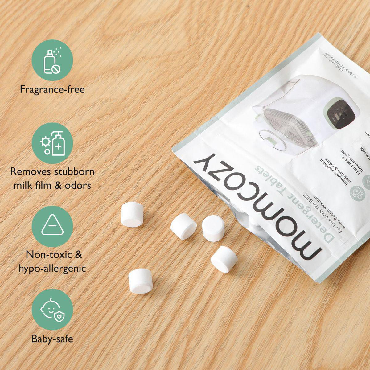 Momcozy Waschmitteltabletten-Verpackung mit losen Tabletten auf Holzoberfläche.
