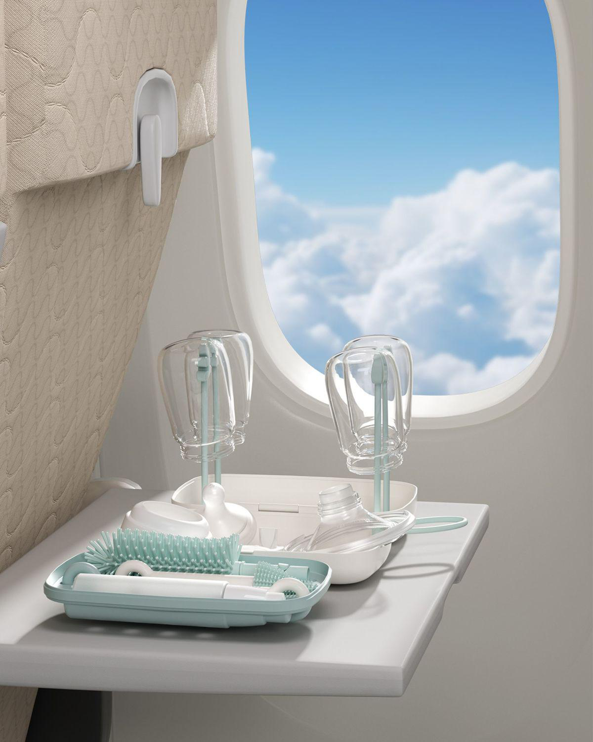 Babyflaschen-Reinigungsset auf einem Flugzeugtablett mit Wolken am Himmel.