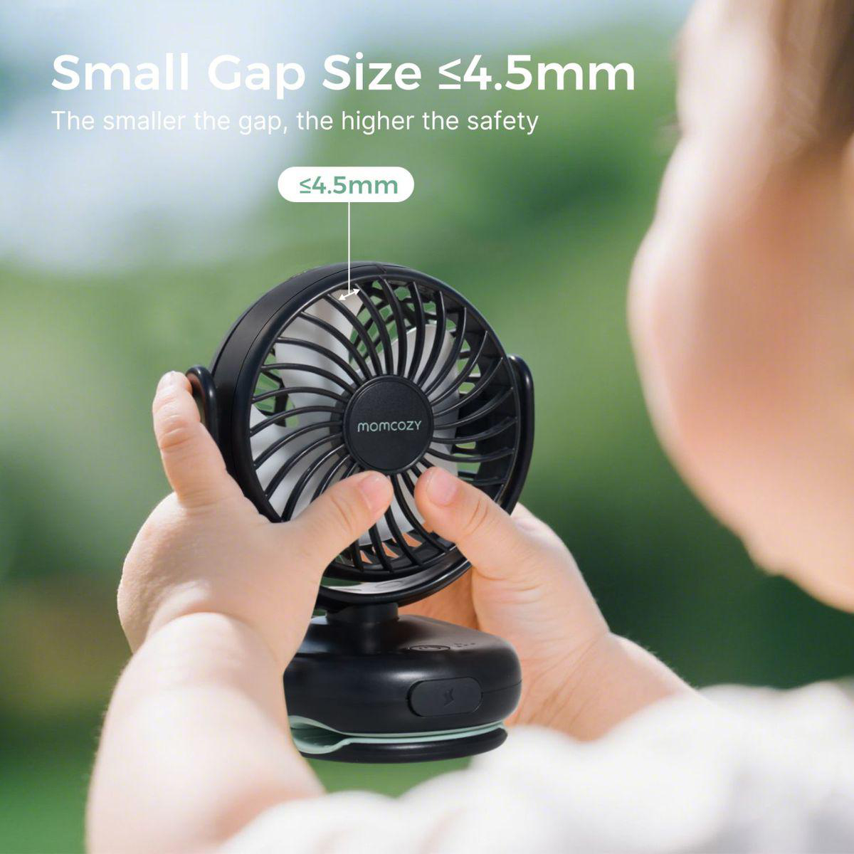 Ein Baby hält einen kleinen schwarzen Ventilator mit der Aufschrift MOMCOZY.