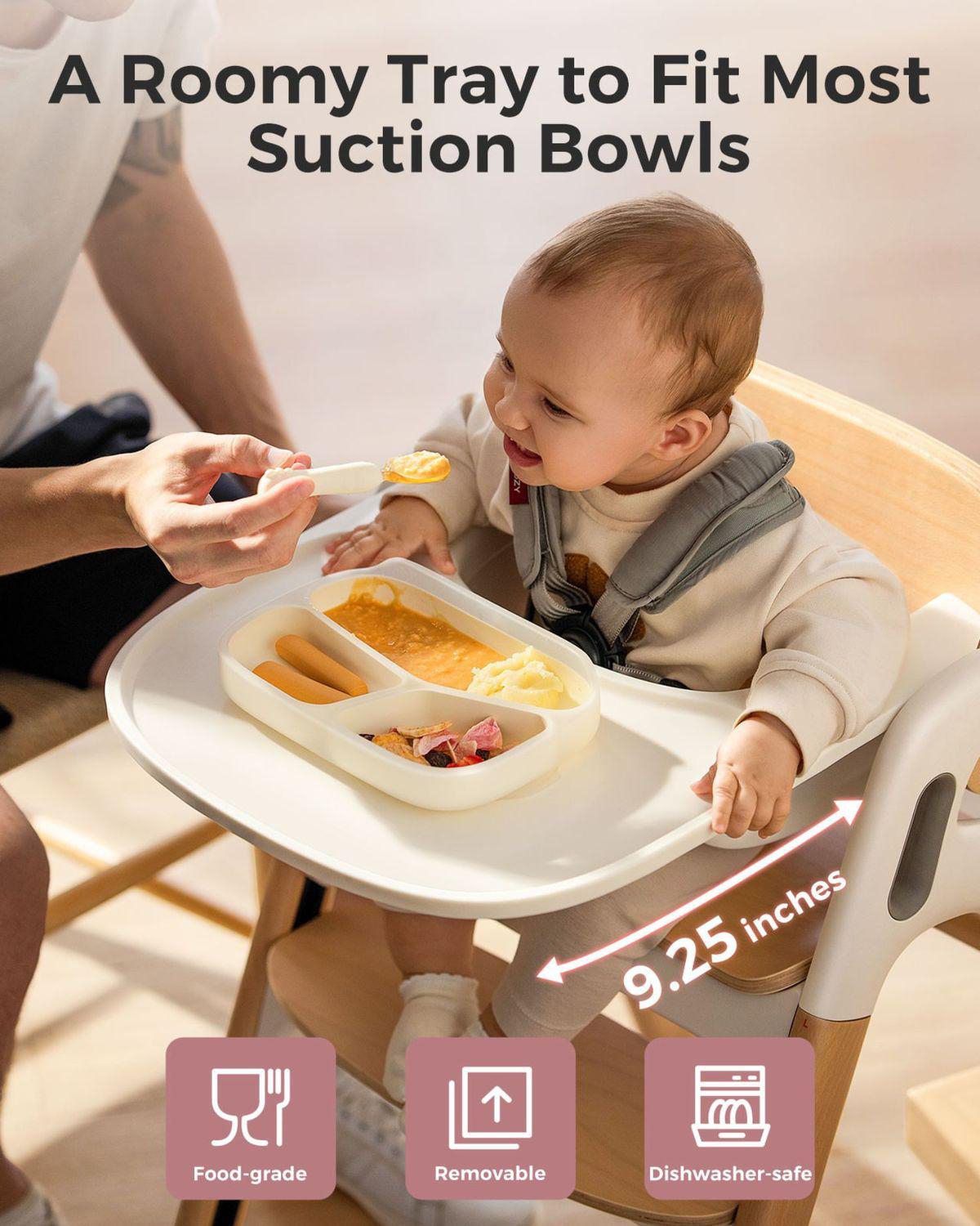 Baby im Hochstuhl wird von Erwachsenem gefüttert. Tablett hat Essen und Saugnäpfe.