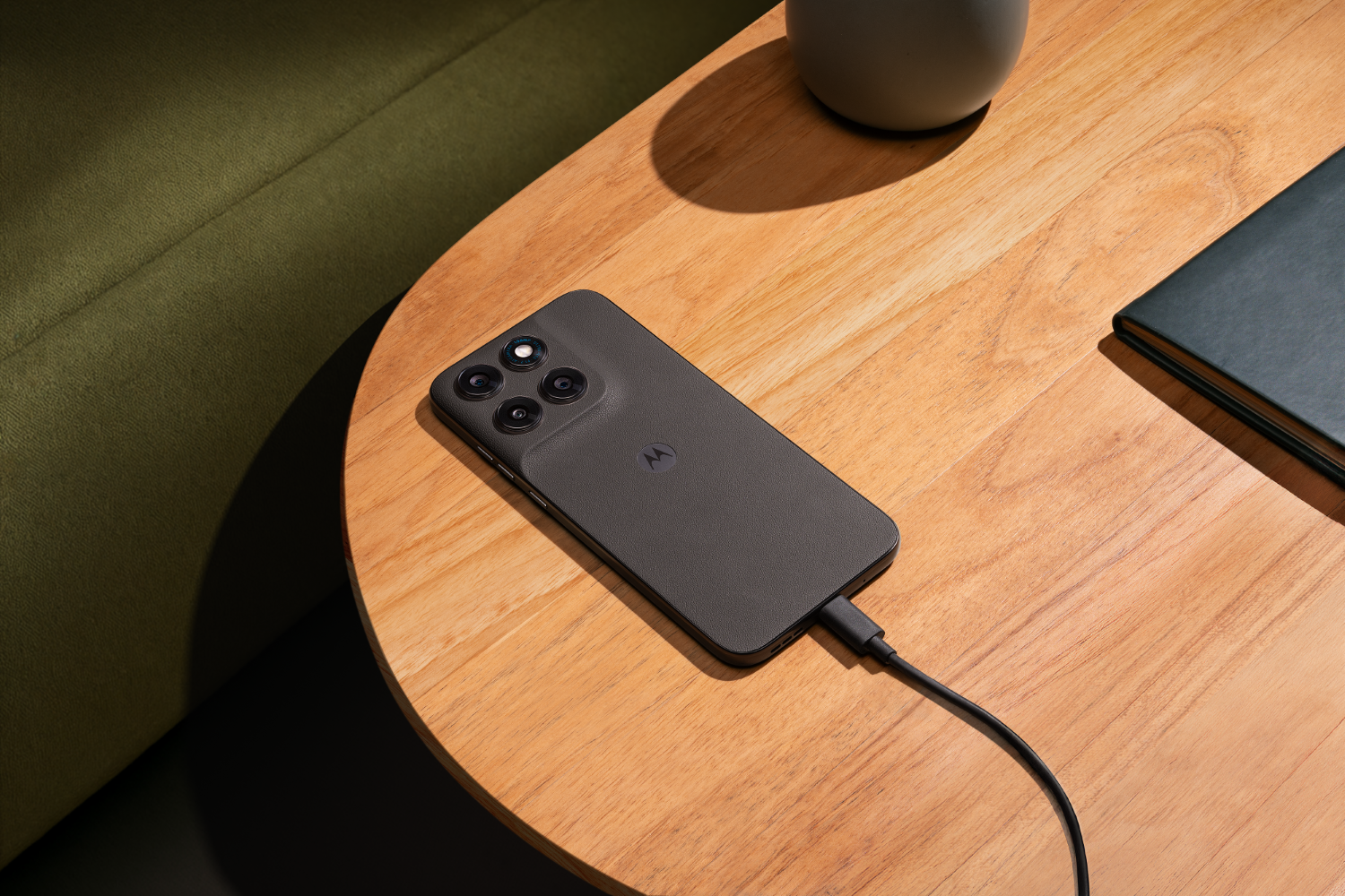 Ciemny telefon Motorola ładuje się na drewnianym stole obok notatnika.