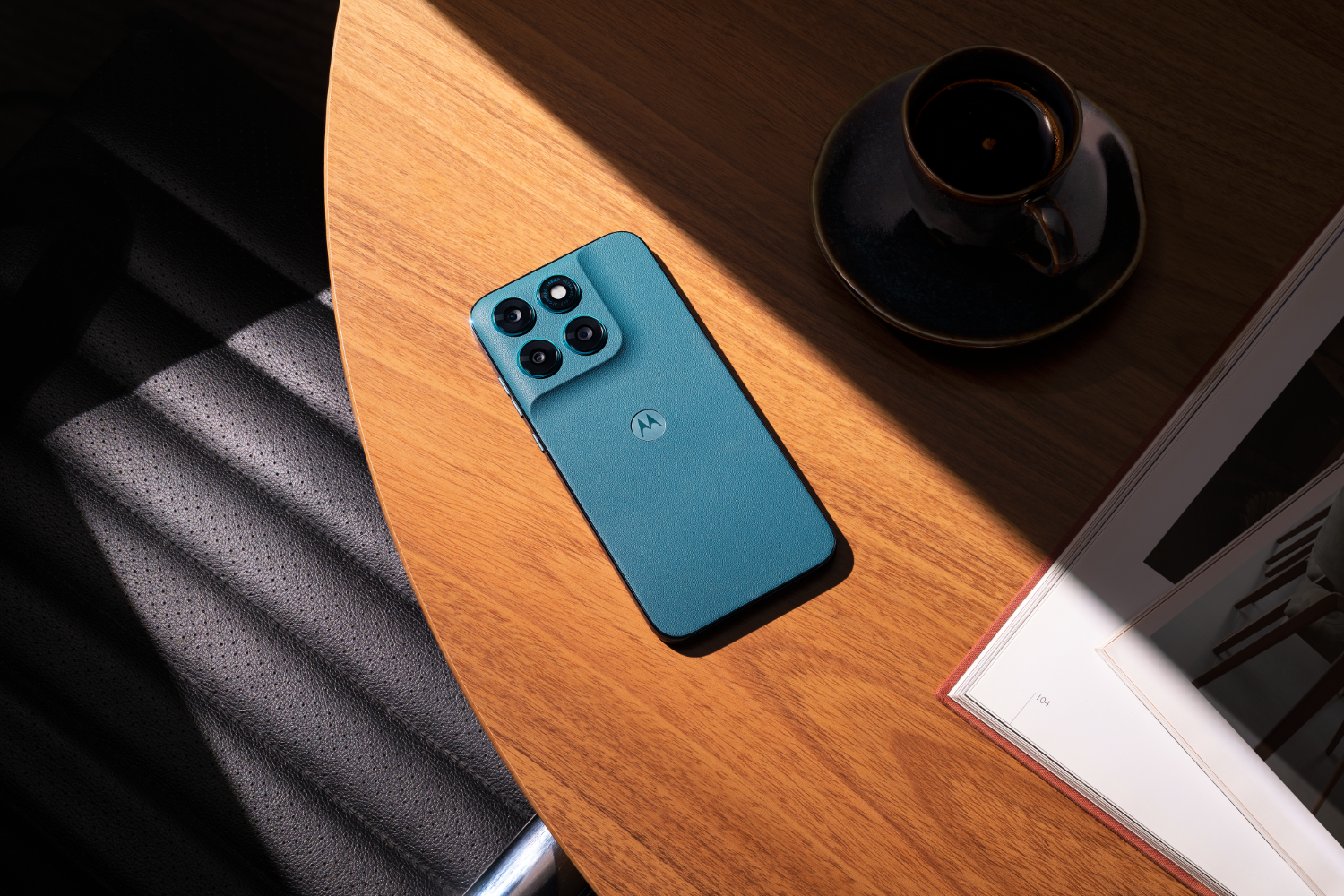 Niebiesko-zielony telefon Motorola leży na drewnianym stole obok filiżanki kawy i książki.