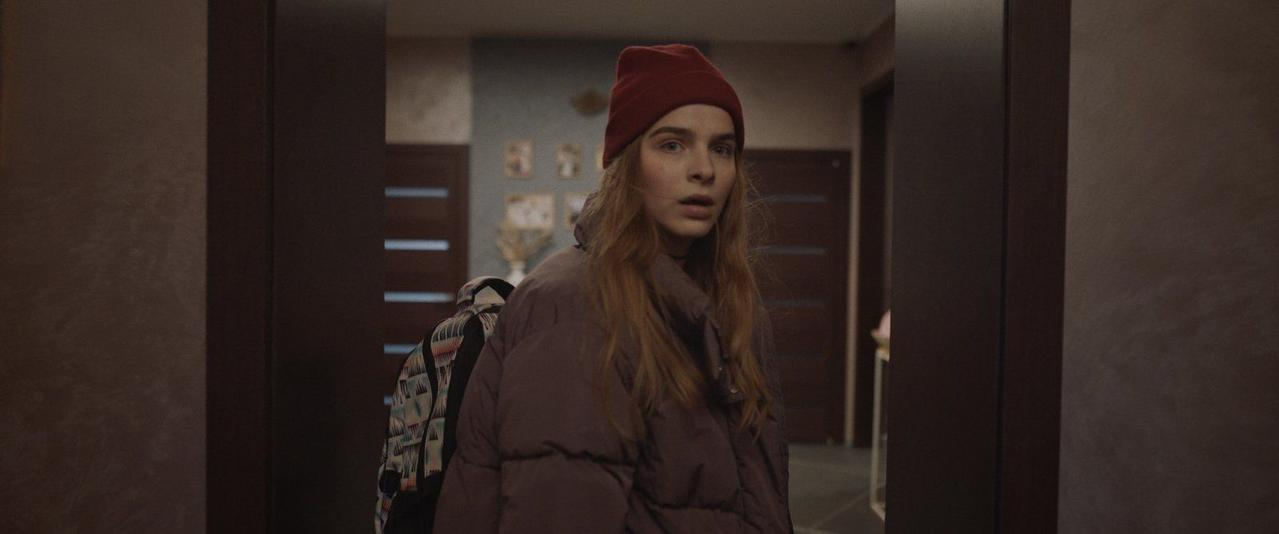 Eine junge Frau mit roter Mütze und Daunenjacke trägt einen bunten Rucksack.