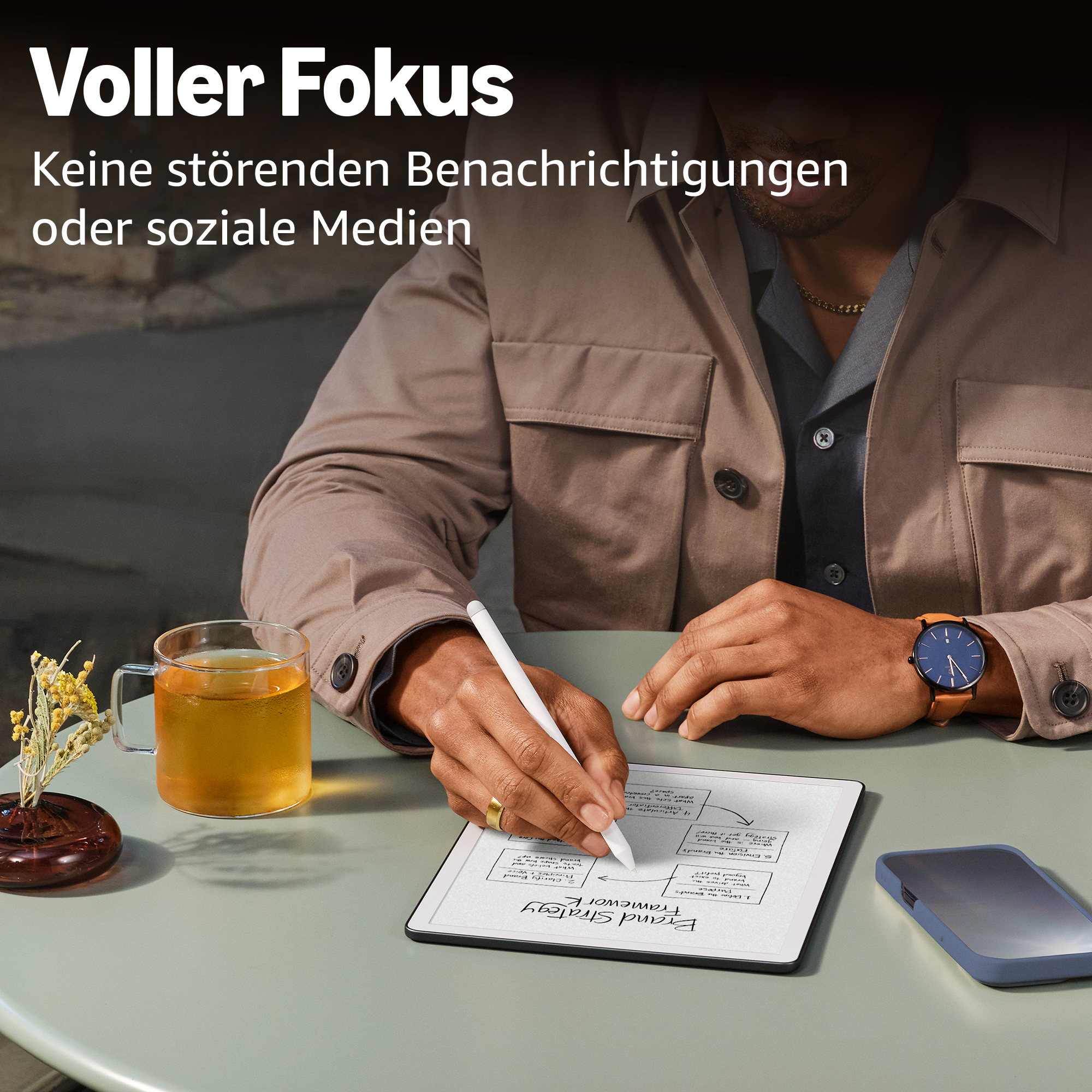 Mann schreibt auf Tablet, daneben Tee und Handy. Fokus auf Arbeit.