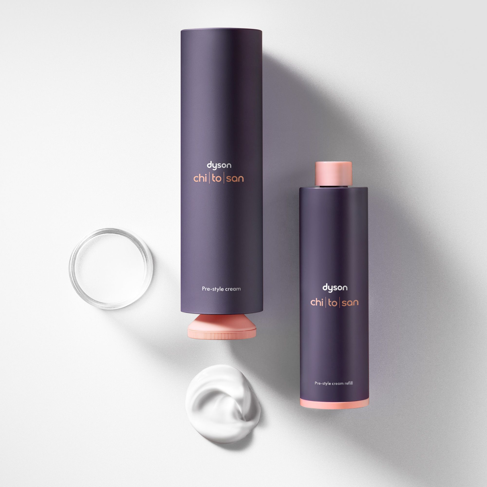 Zwei Dyson Pre-Style Cream Flaschen und eine Probe weiße Creme auf weißem Hintergrund.