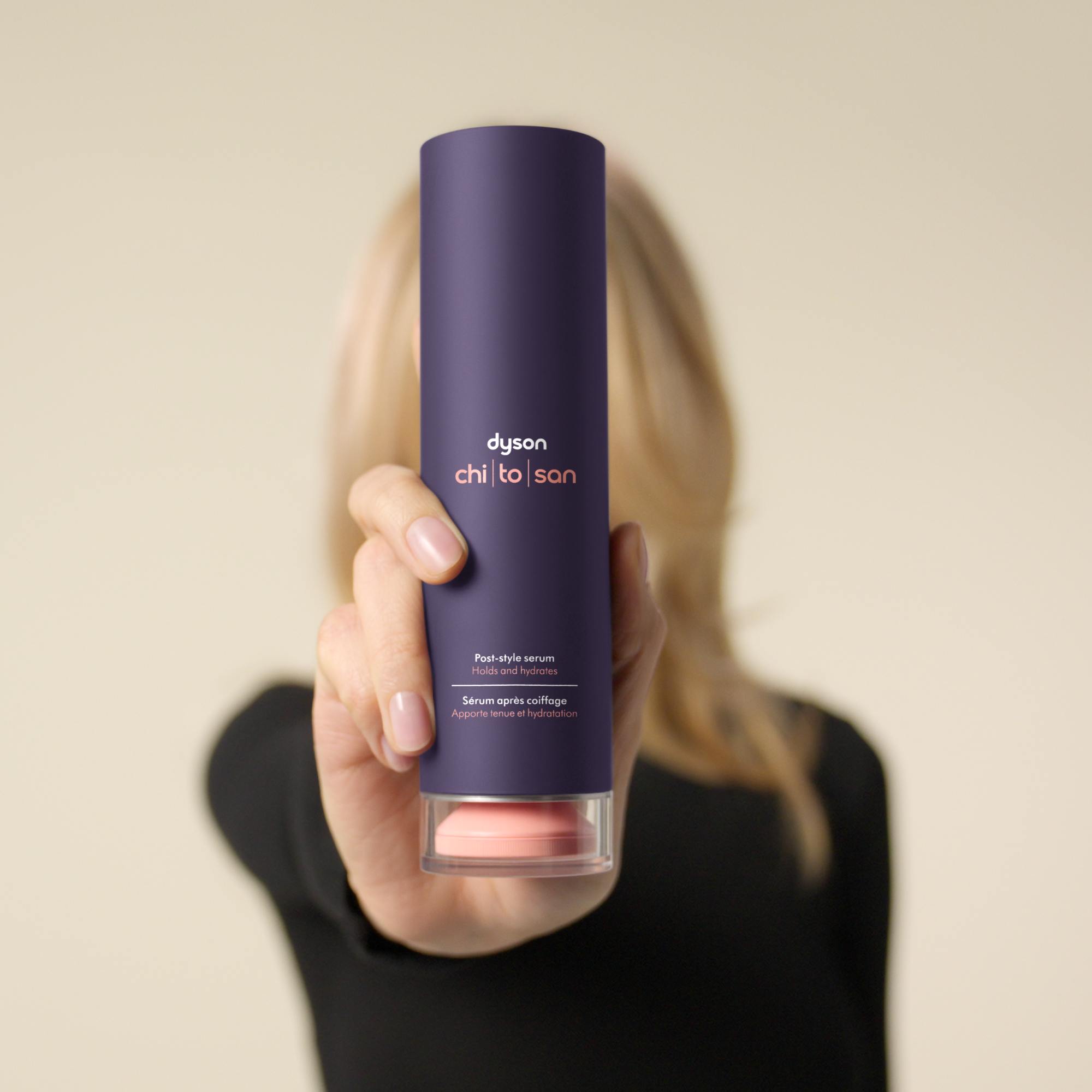 Eine Hand hält eine lila Flasche Dyson-Haarserum mit der Aufschrift „Post-style serum“.