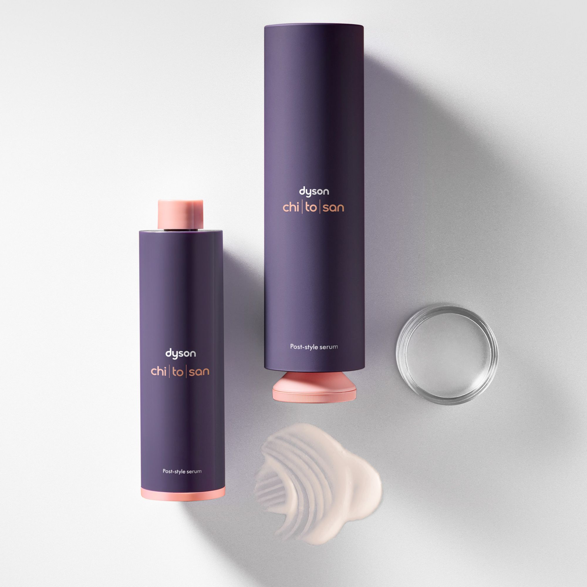 Zwei lila Flaschen mit rosa Kappen und eine Probe eines weißen Serums.