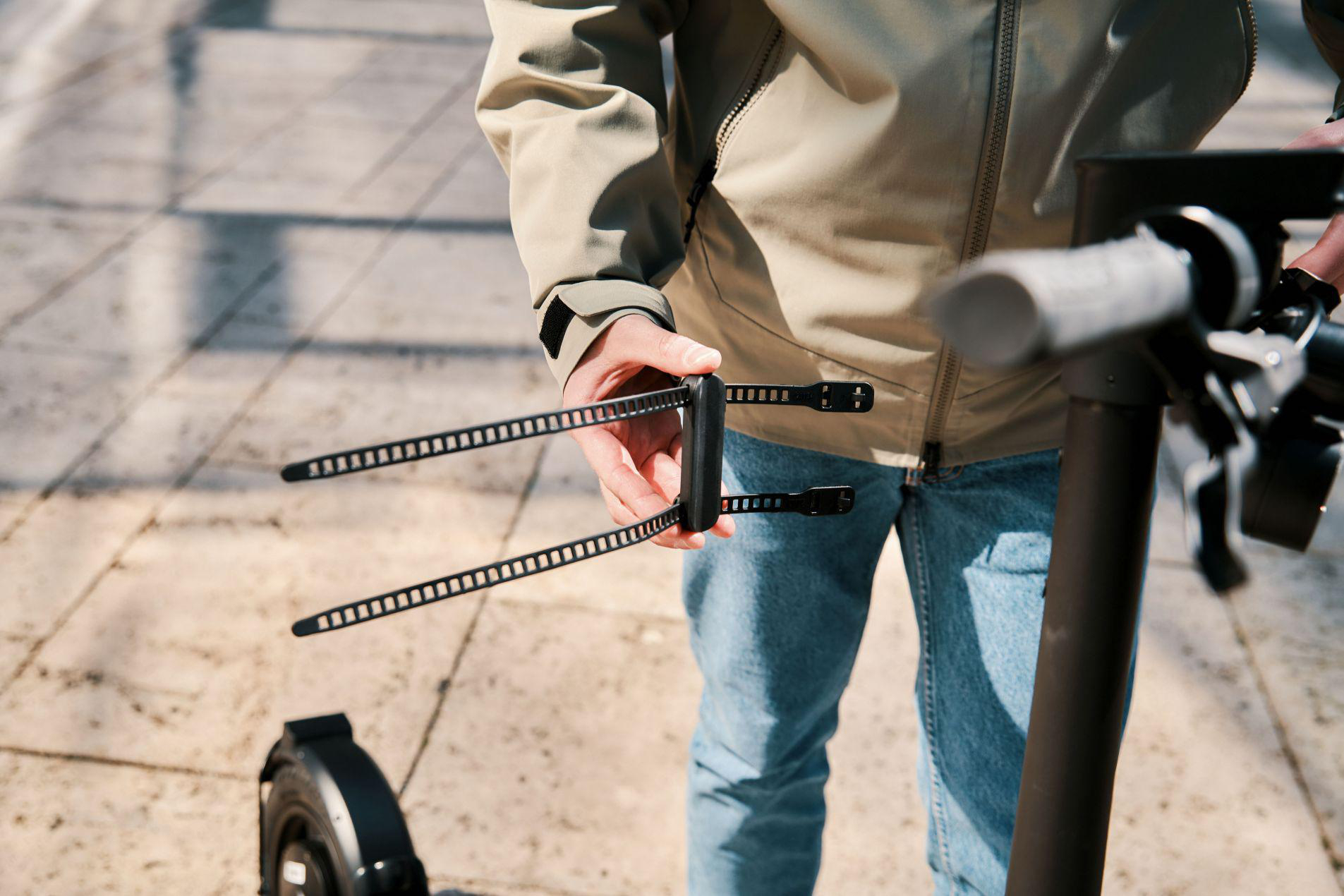 Person hält schwarze Kabelbinder, Elektro-Scooter im Hintergrund.