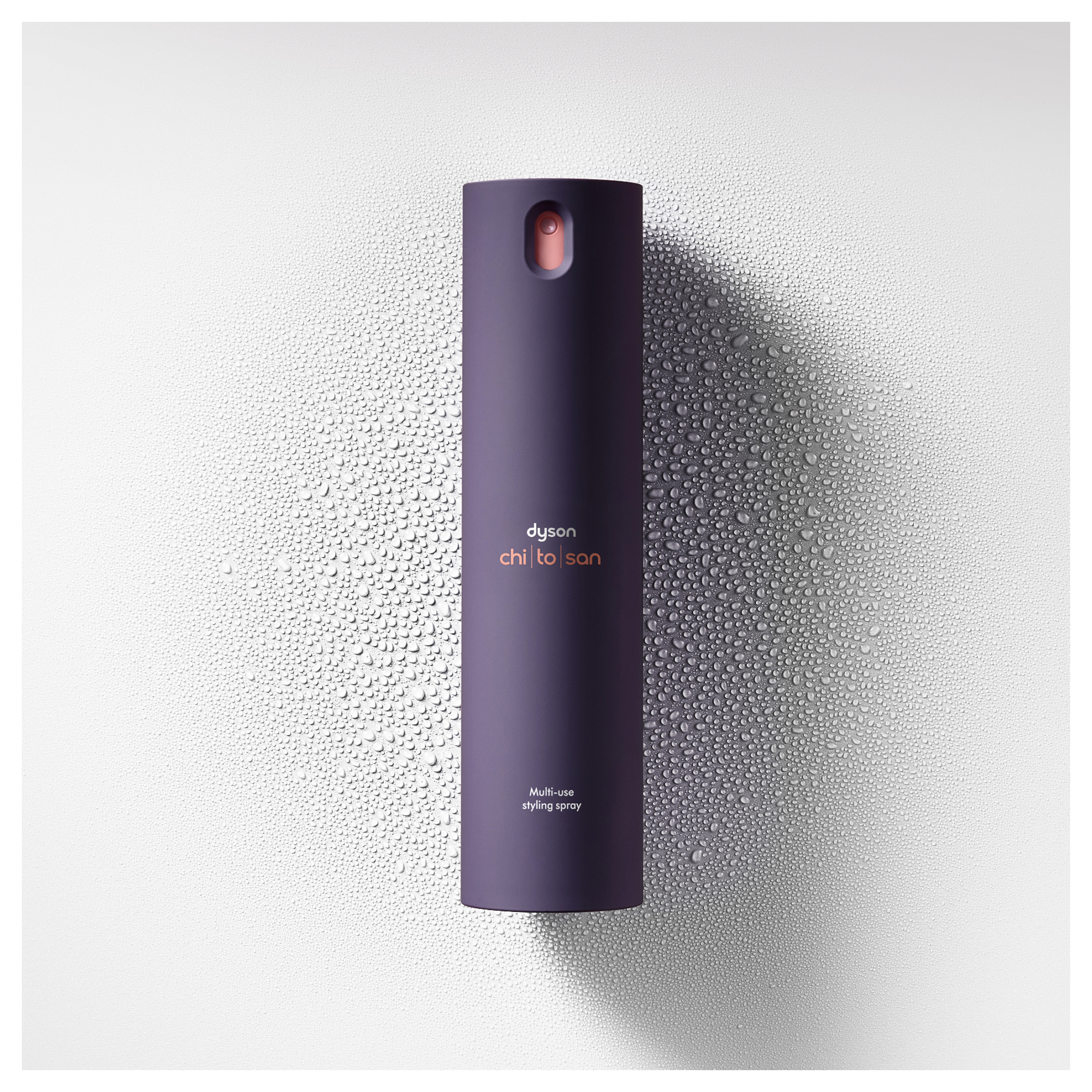 Ein lila Dyson Chi-To-San Styling-Spray steht auf einer nassen, texturierten Oberfläche.