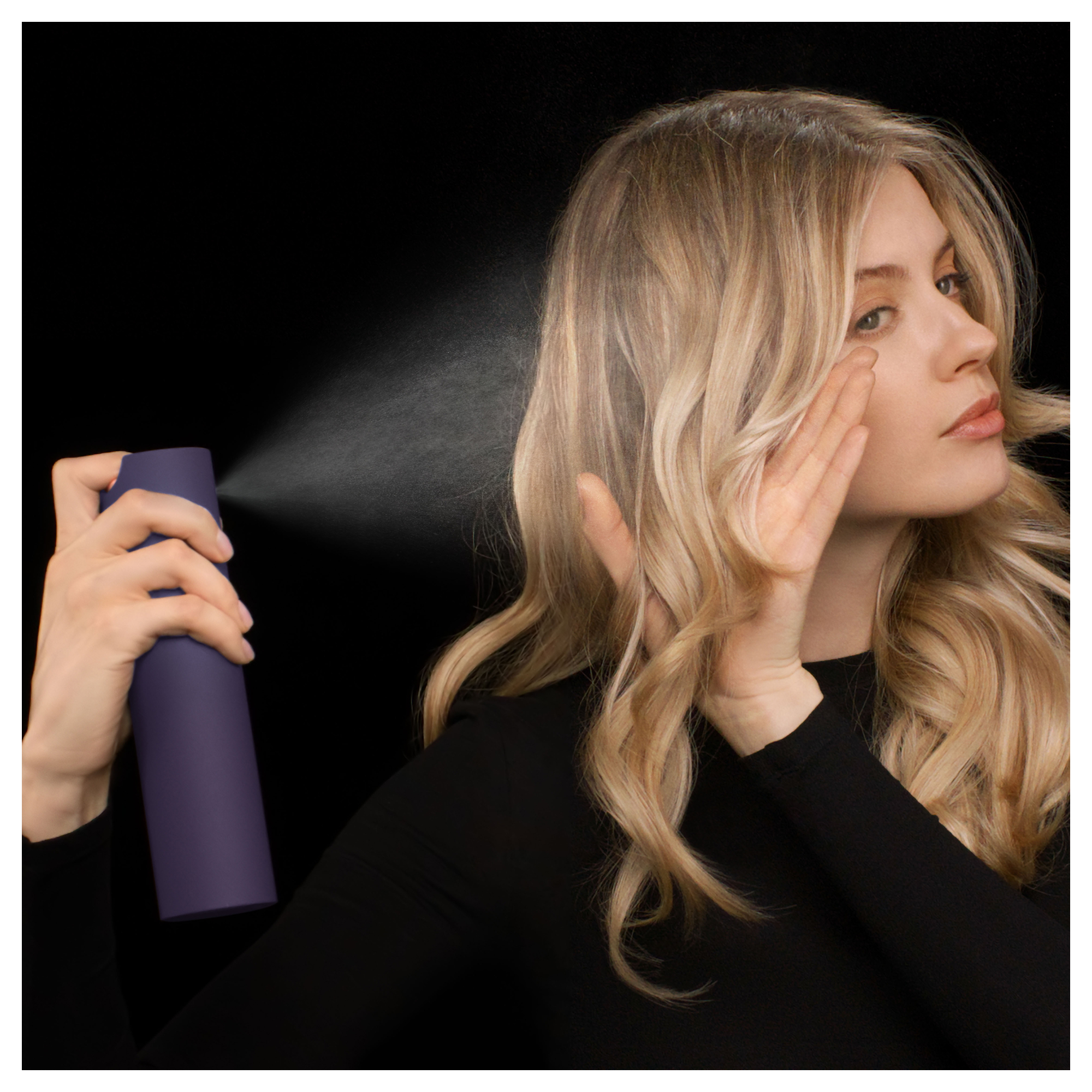 Eine Frau sprüht sich mit Haarspray ins blonde Haar.